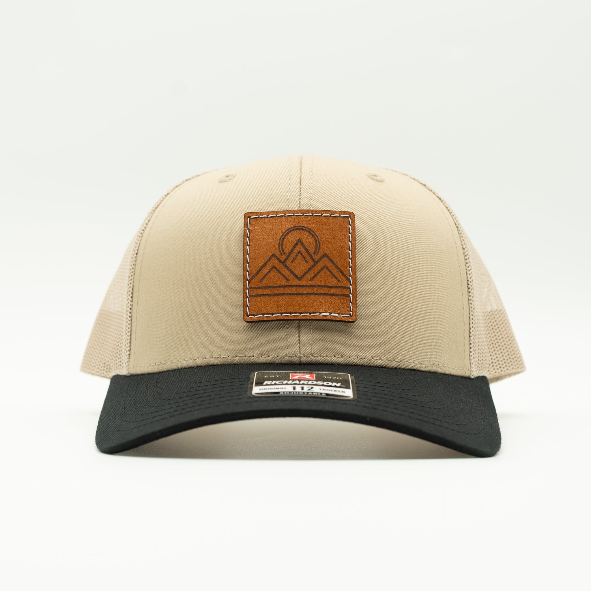 Front view of Lunar Ridge khaki and black combo Richardson 112 trucker hat with leather mountain patch and curved bill