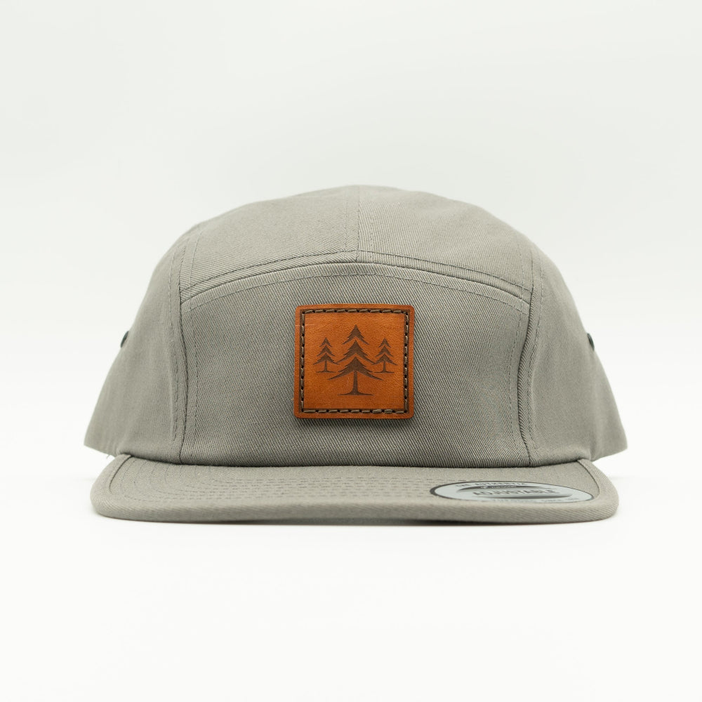 Front view of grey Three Lil Pines leather patch hat on Yupoong 7005, showing square pine tree patch, low-profile five panel crown, and flat bill.