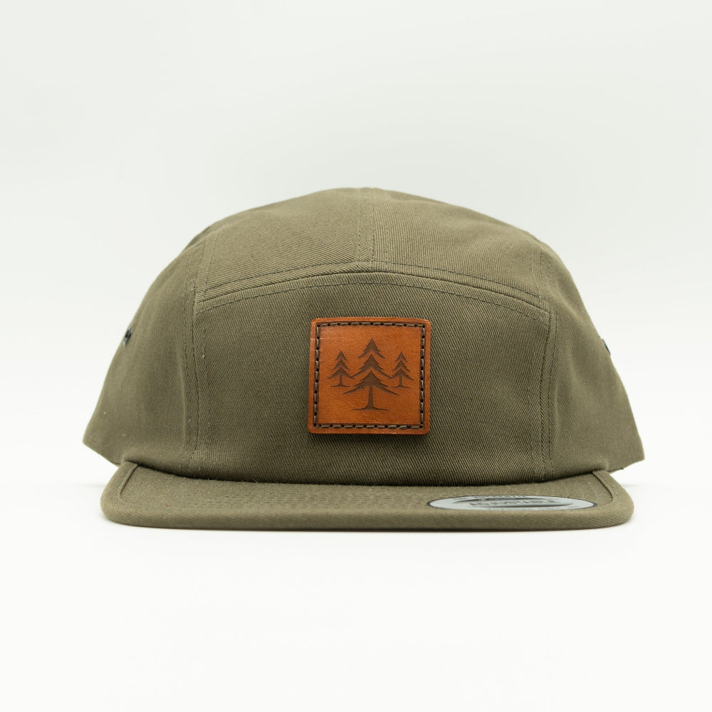 Front view of olive Three Lil Pines leather patch hat on Yupoong 7005, showing square pine tree patch, low-profile crown, and flat bill.