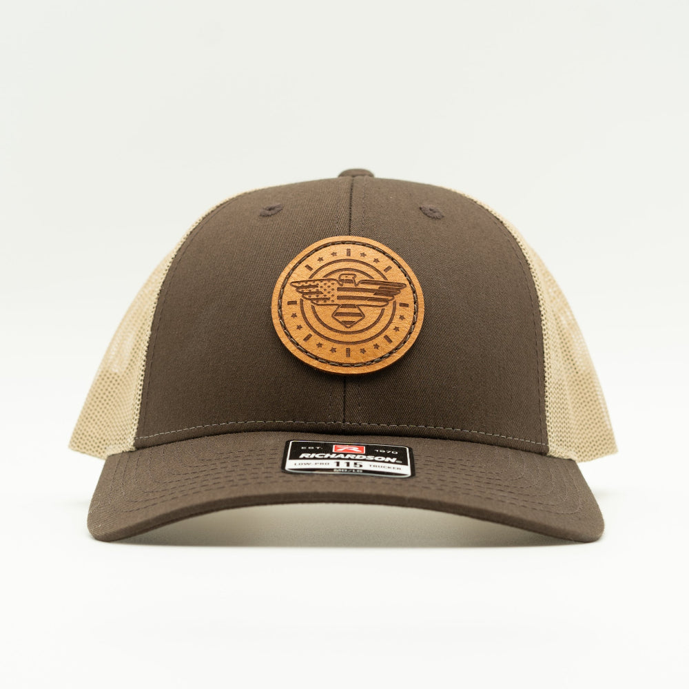 Front view of brown and khaki Richardson 115 low profile trucker hat with American Eagle and flag leather patch, curved visor, and khaki mesh back.
Color: Brown/Khaki
