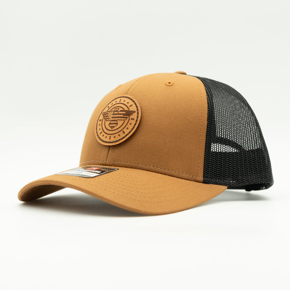 Side view of caramel and black Richardson 115 low profile trucker hat with American Eagle leather patch, showing warm caramel bill, shallow fit, and black mesh back.
Color: Caramel/Black