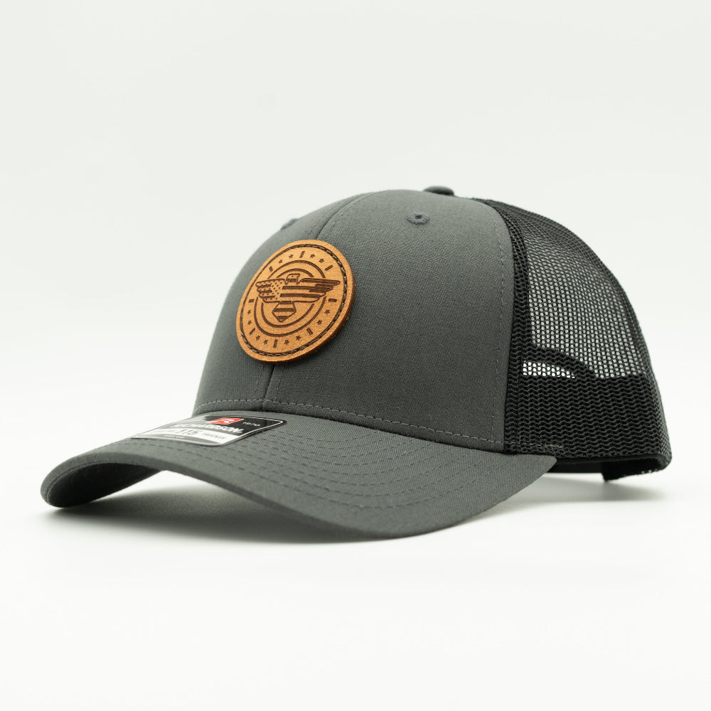 Side view of charcoal and black Richardson 115 low profile trucker hat with American Eagle leather patch, showing curved bill, shallow crown, and black mesh back.
Color: Charcoal/Black