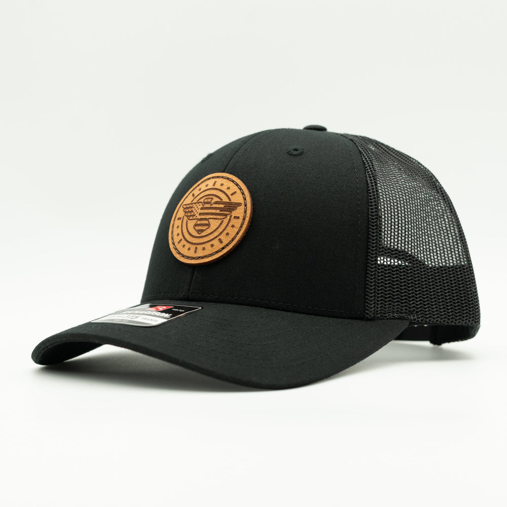 Side view of solid black Richardson 115 low profile trucker hat with American Eagle leather patch, showing shallow crown, curved bill, and black mesh back.
Color: Solid Black