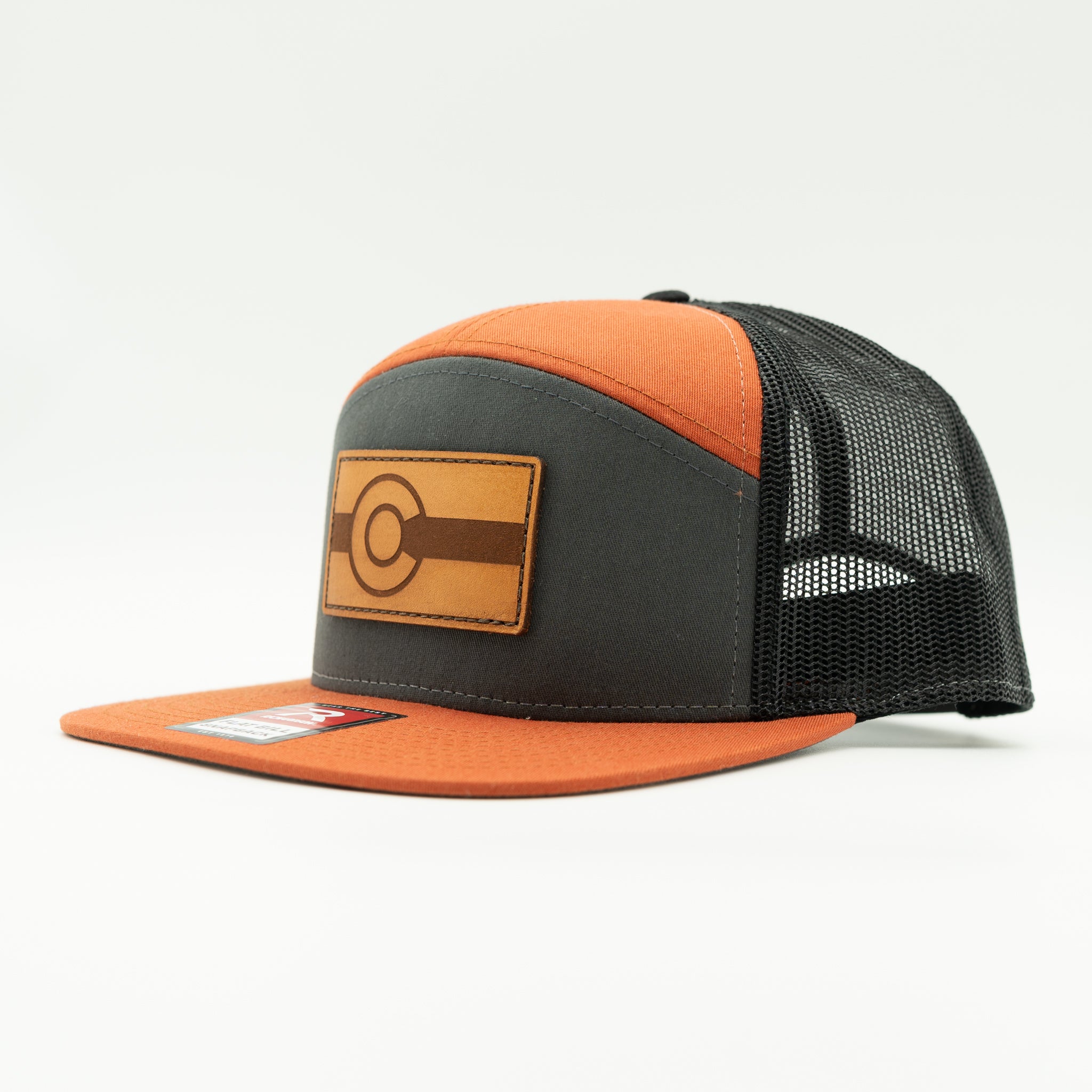 Side view of charcoal and orange Richardson 168 flat bill trucker hat with light brown leather Colorado flag patch, bold Colorful Colorado hat