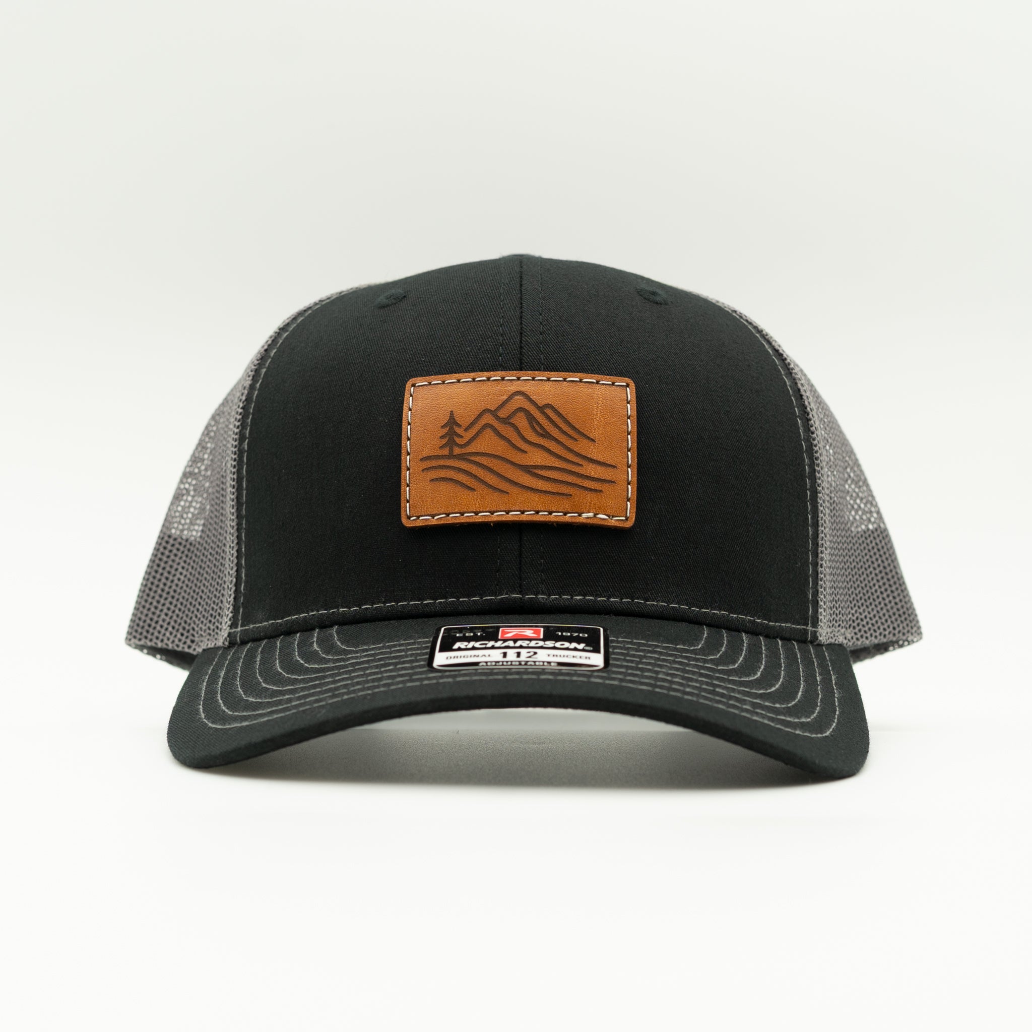 Front view of black and charcoal Richardson 112 Driftline leather patch trucker, structured mid profile mountain cap