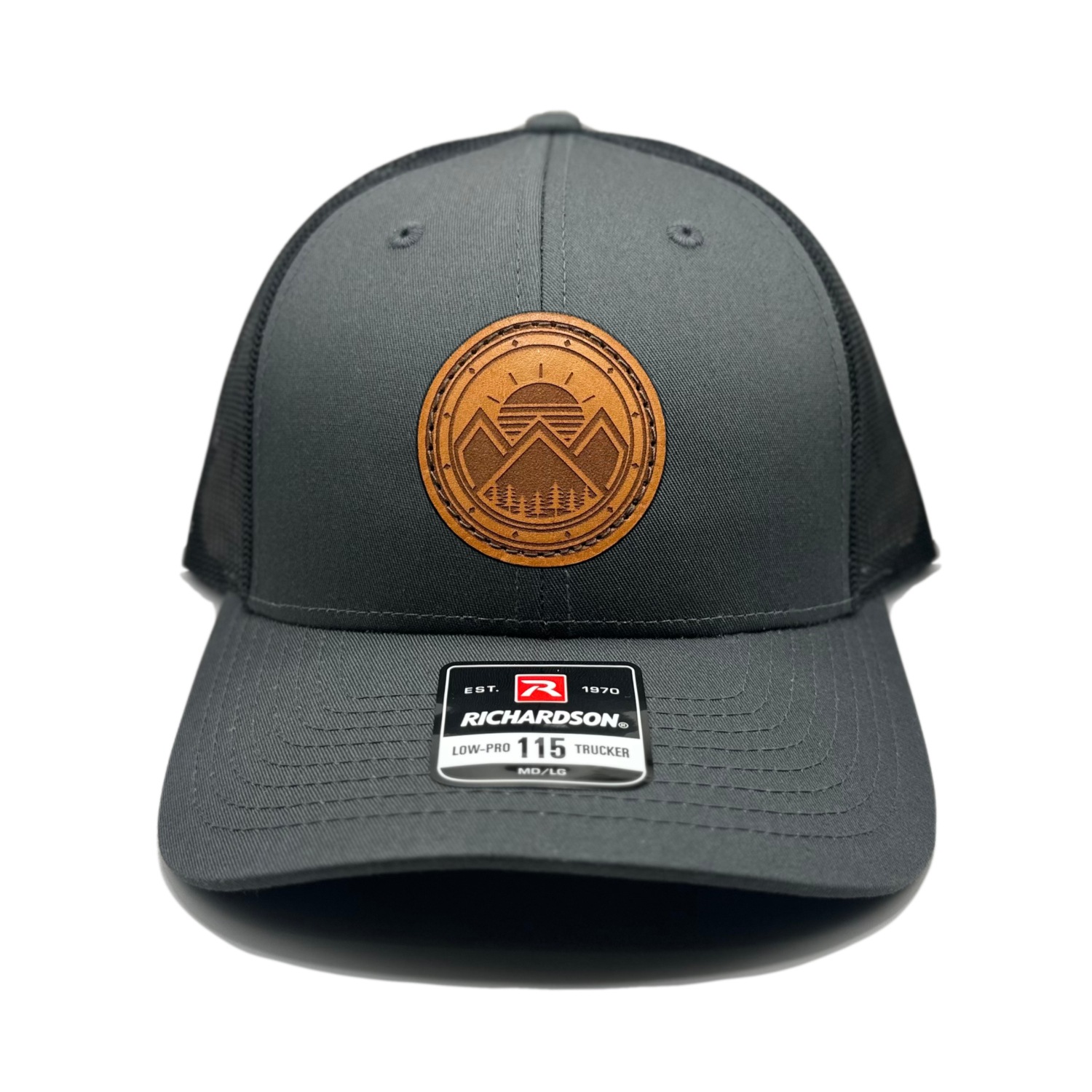A unique leather patch hat called Modern Mountains, featuring a one-of-a-kind design with 3 mountain peaks, a sunrise, pine trees, and decorative border on a circular patch. Made in the USA, this authentic leather patch is sewn onto a SnapBack adjustable hat. Available in small and m/l sizes in the Richardson 115 style, and multiple colors in the Richardson 112. Inspired by the mountainous surroundings of our Colorado location, this hat is perfect for those who appreciate high-quality, stylish leather patch