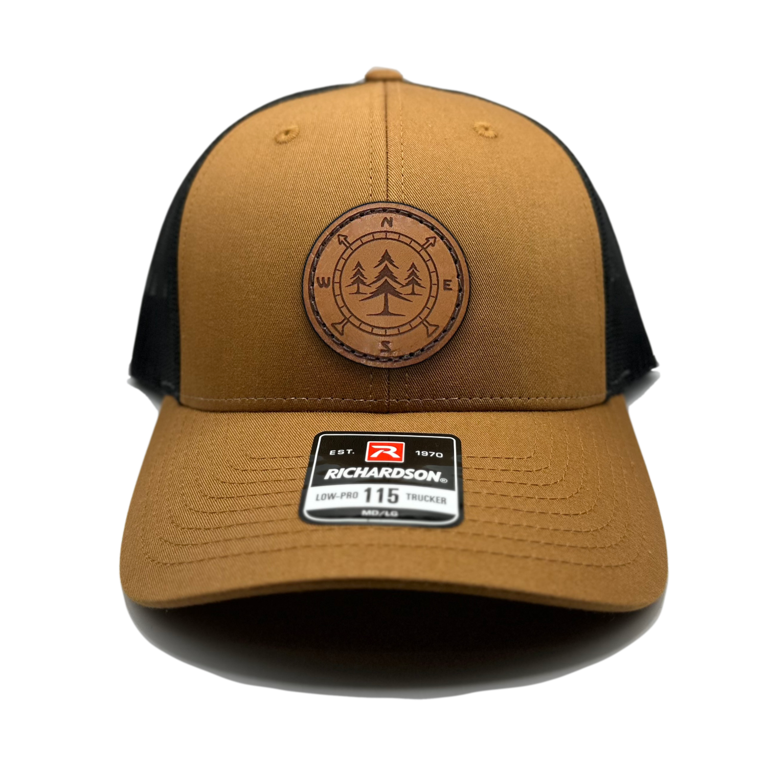 A close-up photo of a leather patch hat called Lost Pines. The hat features a unique compass and pine trees design on a circular leather patch that is sewn onto the front. The hat is a Carmel/black Richardson 115 low profile SnapBack adjustable hat, made in the USA. Available m/l sizes and multiple colors. Inspired by the mountains of Colorado, USA. 