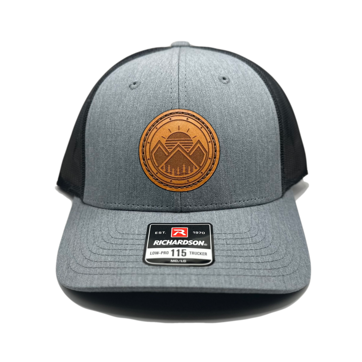 A trendy leather patch hat named Modern Mountains, boasting a unique design with three mountain peaks, a sunrise, pine trees, and a decorative border on a circular patch. Crafted and designed in the USA, this authentic leather patch is skillfully sewn onto a SnapBack adjustable hat. Offered in small and m/l sizes in the Richardson 115 style, as well as multiple colors in the Richardson 112. Inspired by the picturesque surroundings of our Colorado mountain location, this hat is perfect for fashion-forward