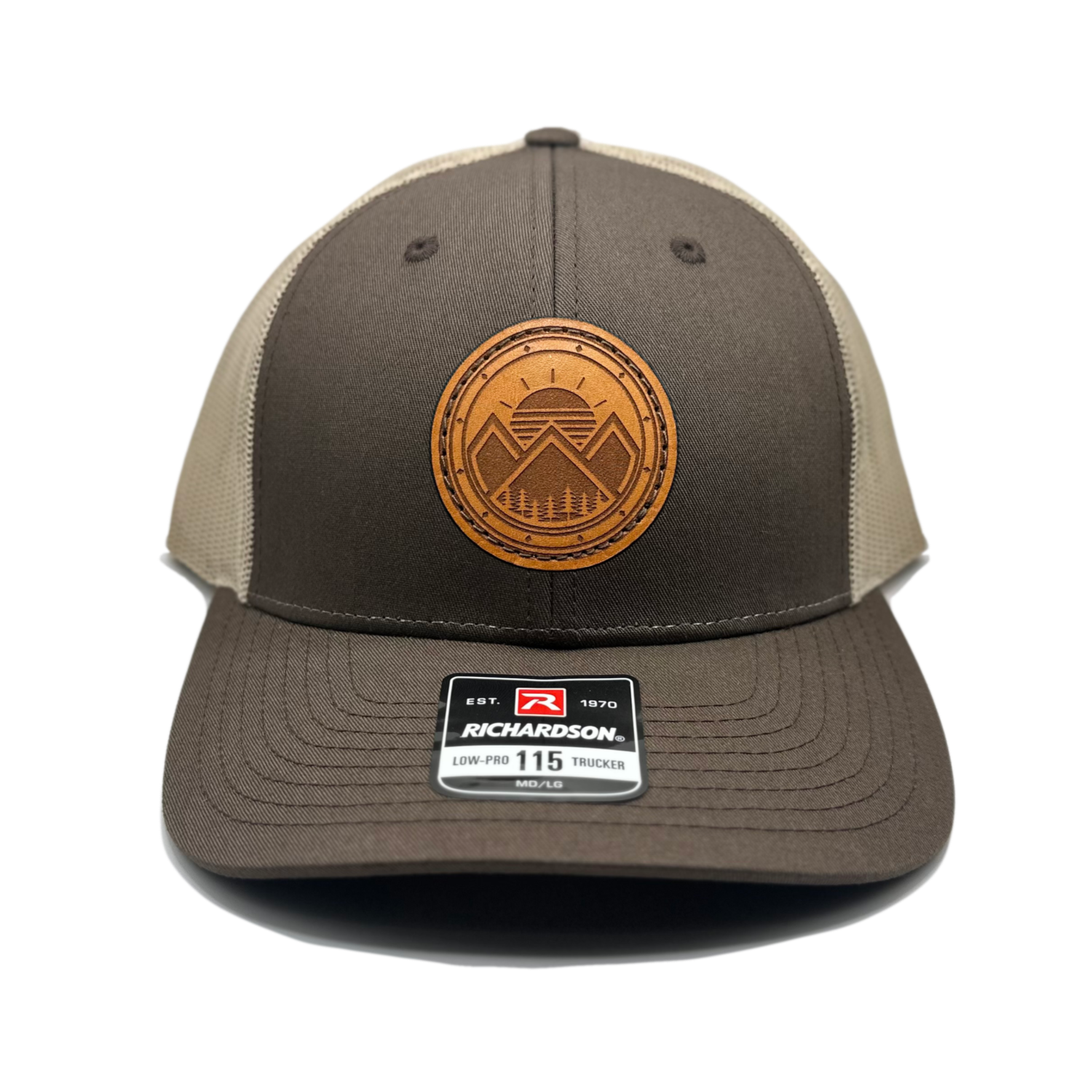 A unique leather patch hat called Modern Mountains, featuring a one-of-a-kind design with 3 mountain peaks, a sunrise, pine trees, and decorative border on a circular patch. Made in the USA, this authentic leather patch is sewn onto a SnapBack adjustable hat. Available in small and m/l sizes in the Richardson 115 style, and multiple colors in the Richardson 112. Inspired by the mountainous surroundings of our Colorado location, this hat is perfect for those who appreciate high-quality, stylish leather patch