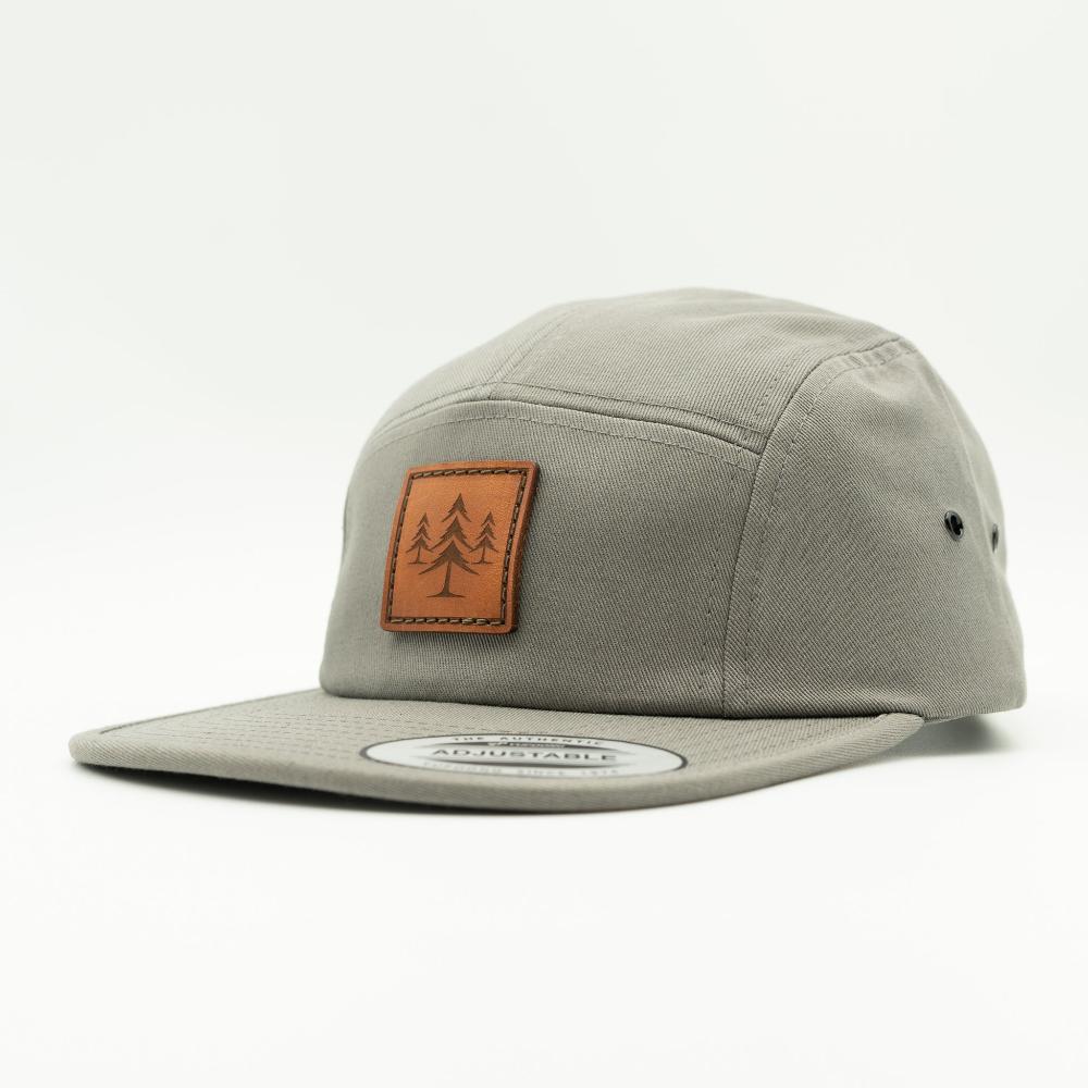 Side view of grey Yupoong 7005 Three Lil Pines hat, showing soft cotton panel, flat bill, and sewn real leather pine tree patch.
