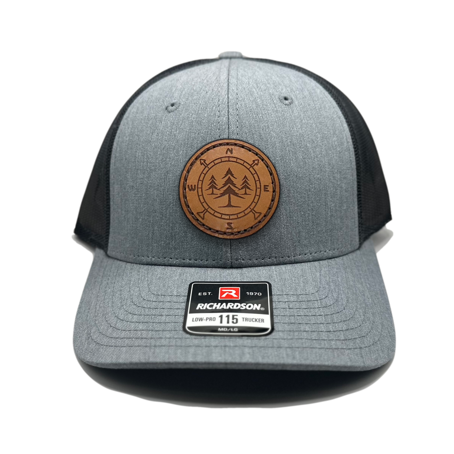 A high-quality leather patch hat named Lost Pines, showcasing a distinctive compass and pine trees design on a circular leather patch. Made in the USA, this hat features genuine leather craftsmanship and is affixed to a Heather grey/charcoal Richardson 115 low profile SnapBack hat. Available in small and m/l sizes and various colors, this unique hat is inspired by the picturesque mountains of Colorado. Perfect for hat enthusiasts and those seeking stylish leather patch designs.