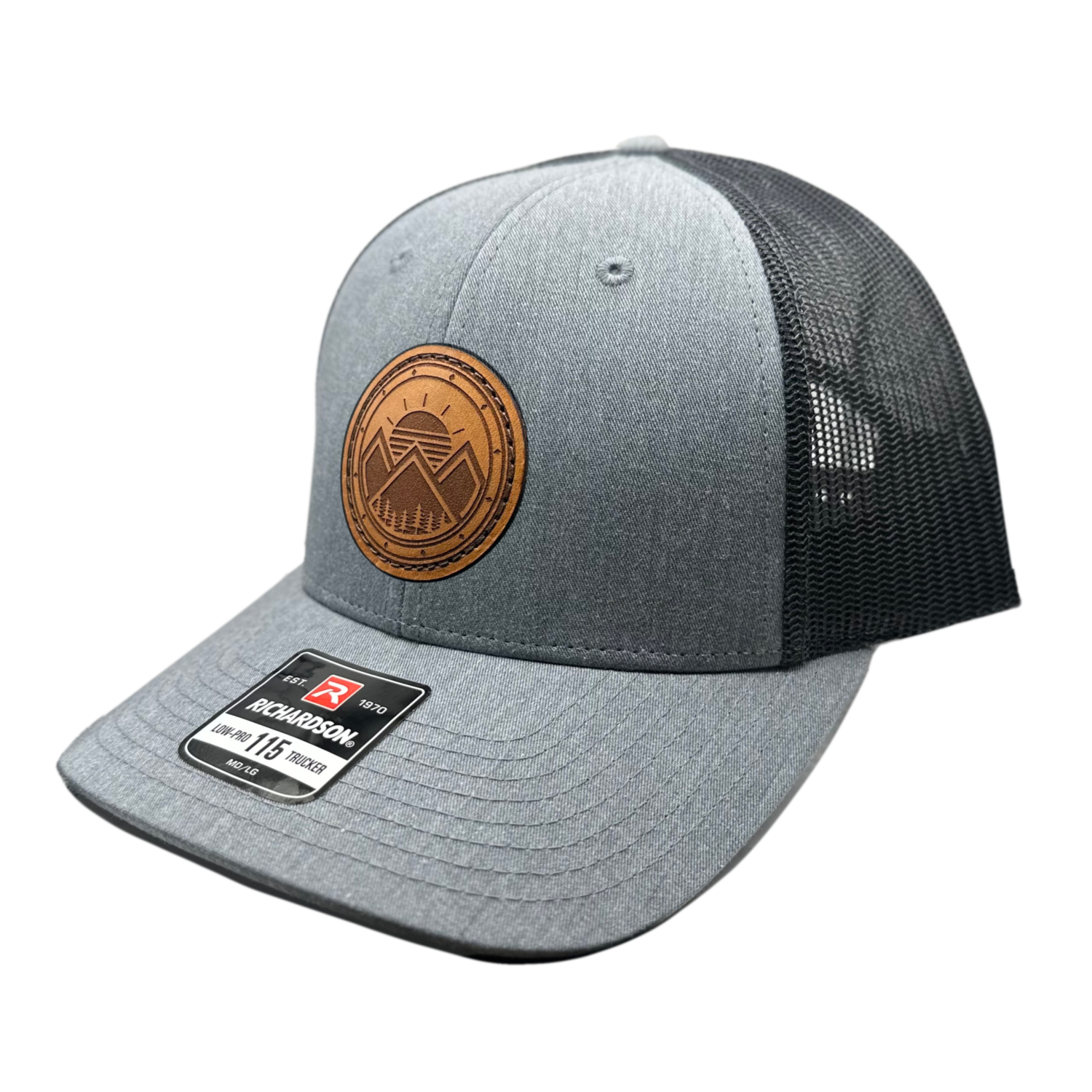 A trendy leather patch hat named Modern Mountains, boasting a unique design with three mountain peaks, a sunrise, pine trees, and a decorative border on a circular patch. Crafted and designed in the USA, this authentic leather patch is skillfully sewn onto a SnapBack adjustable hat. Offered in small and m/l sizes in the Richardson 115 style, as well as multiple colors in the Richardson 112. Inspired by the picturesque surroundings of our Colorado mountain location, this hat is perfect for fashion-forward in