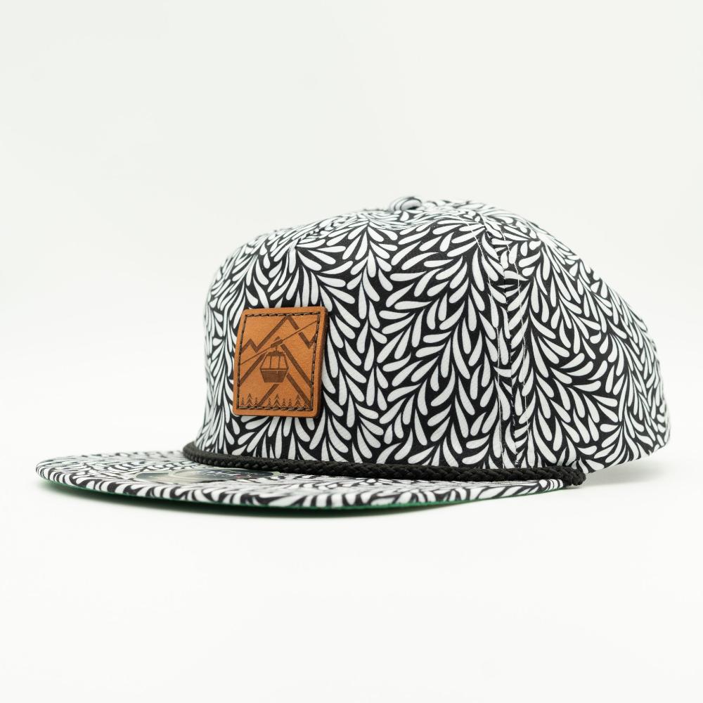 A flat-brim snapback cap featuring a black and white leaf pattern, with a brown leather patch on the front displaying a mountain and cable car graphic.
Color: Throwback Black