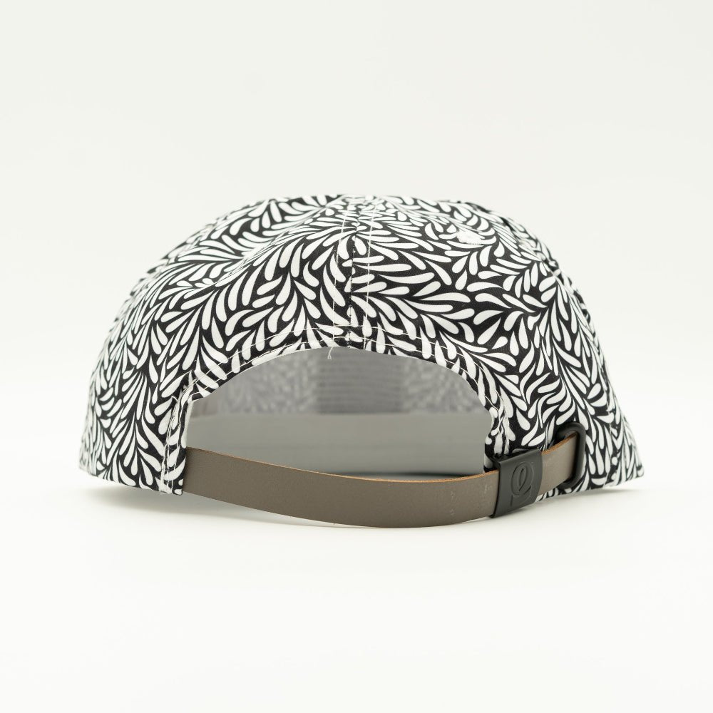 A baseball cap shown from the back, featuring a black and white leaf pattern on the crown and a brown adjustable strap.
Color: Throwback Black
