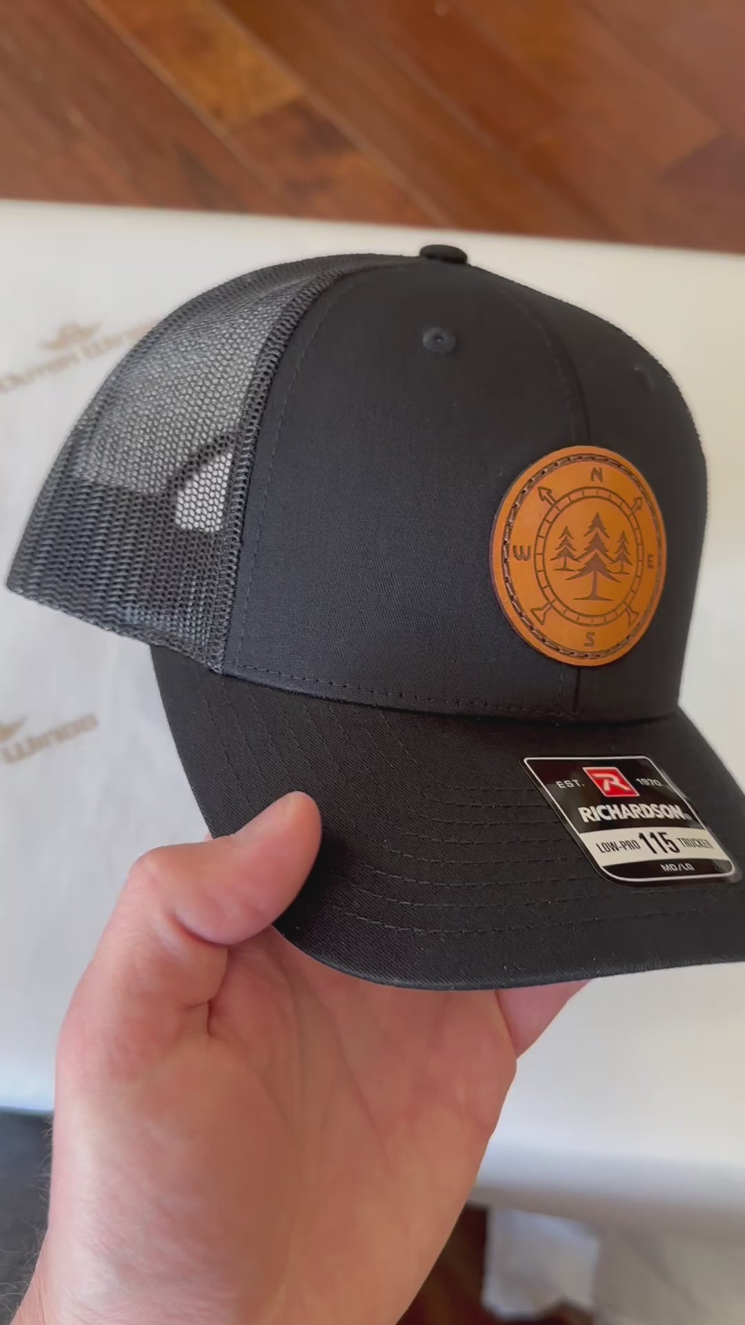 A premium custom leather patch hat named Lost Pines, showcasing a distinctive compass and pine trees design on a circle patch. Handcrafted in the USA, this unique hat features authentic leather stitching on a Richardson 115 low profile SnapBack hat. Available in small and m/l sizes in a variety of colors, this hat is inspired by the scenic mountains of Colorado. Perfect for hat enthusiasts seeking high-quality custom leather patch designs.