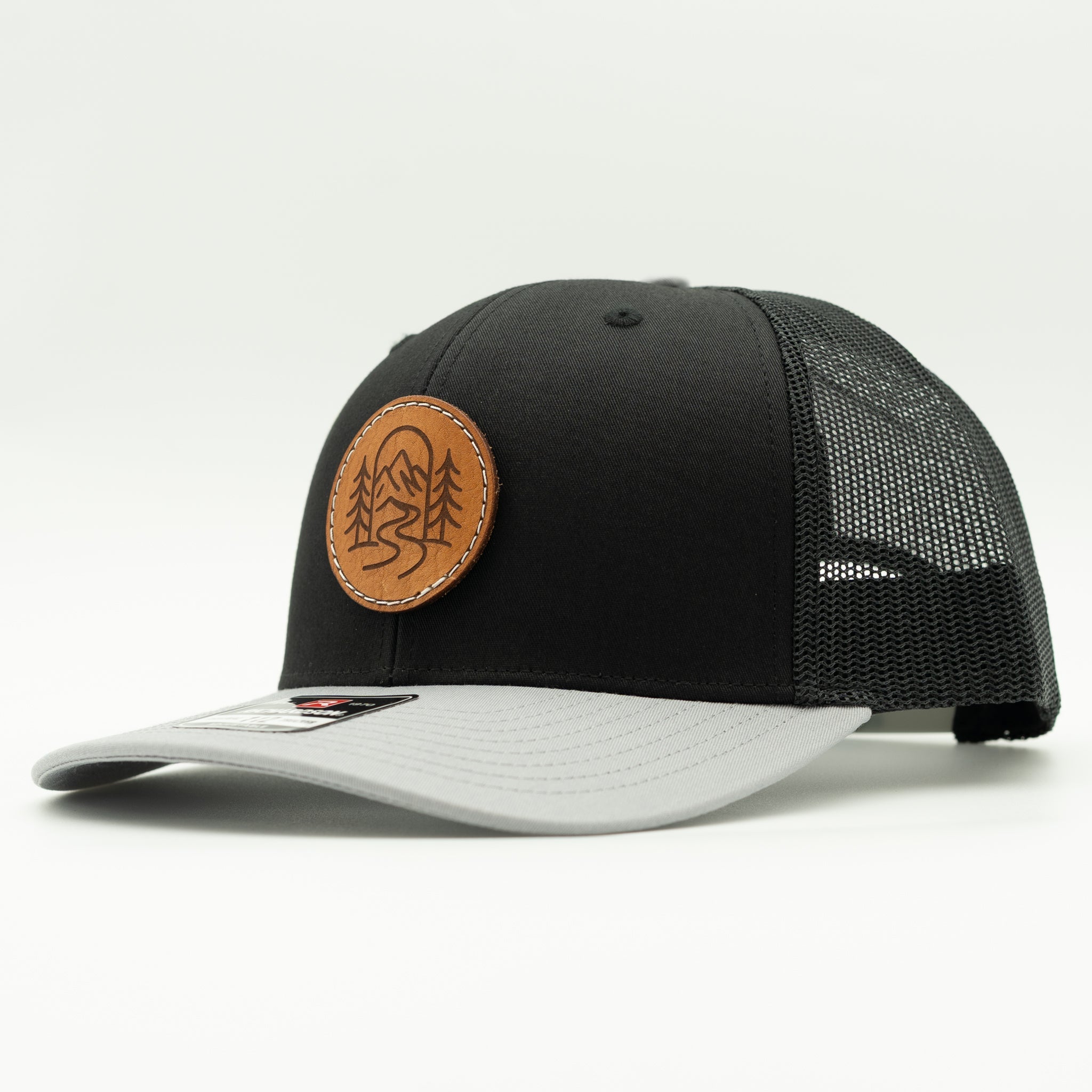 Side view of The Passage black and grey Richardson 112 leather patch mountain trucker hat.