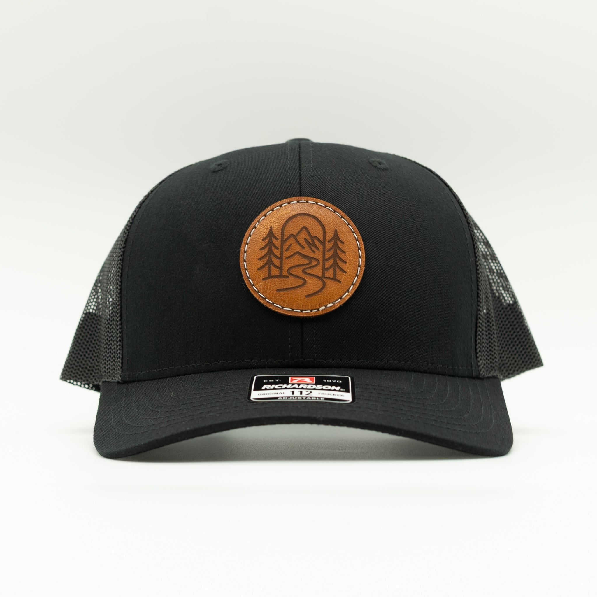 Front view of solid black Richardson 112 The Passage trucker hat with round engraved leather patch.