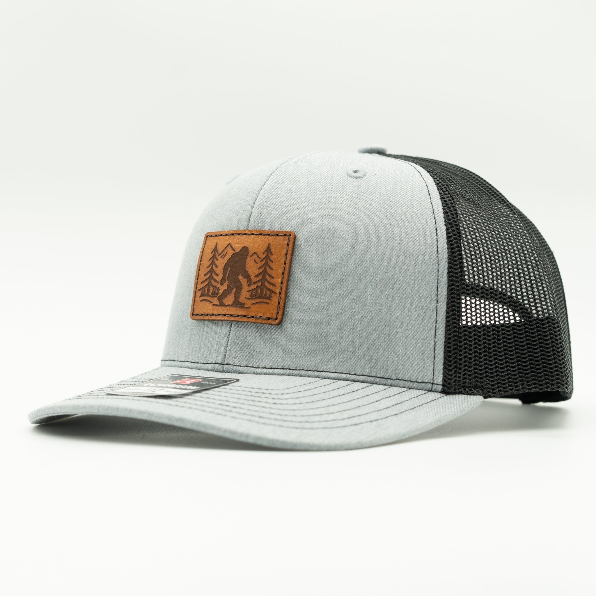 Side view of heather grey front, black mesh Mountain Myth Richardson 112 hat with engraved Bigfoot leather patch for mountain hat style.