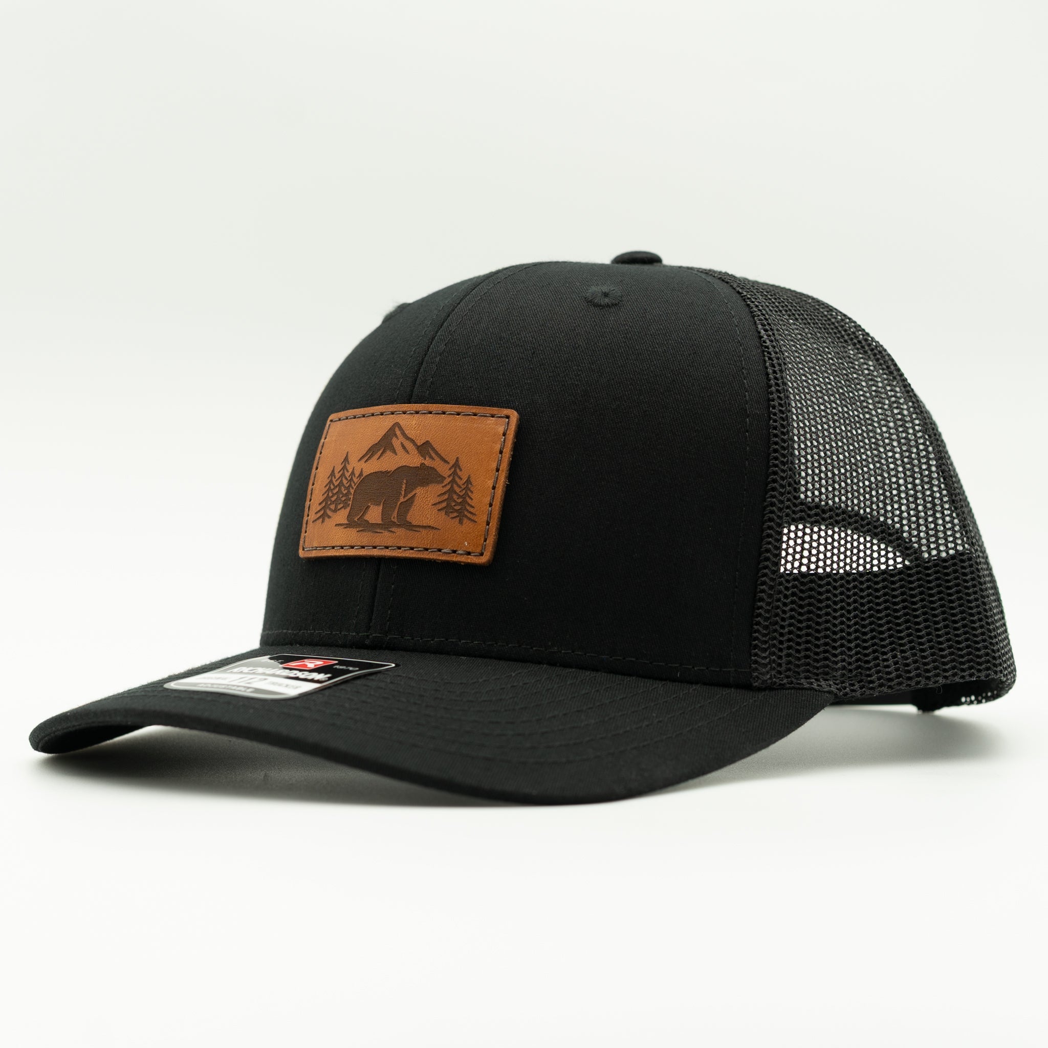 Side view of Bearline Peak leather patch hat on solid black Richardson 112, highlighting engraved bear and pine tree leather patch, curved visor, and breathable mesh back.
Color: Solid Black