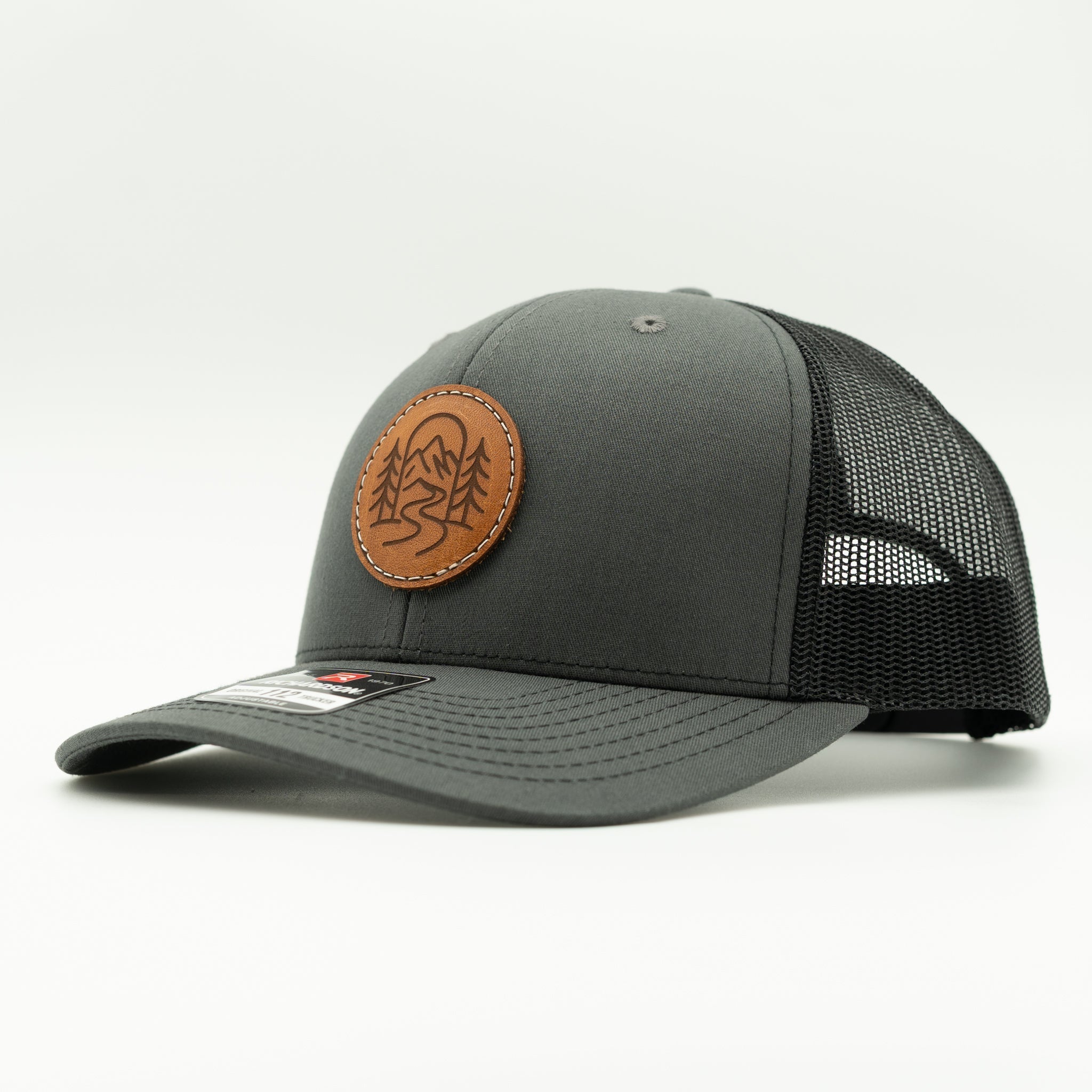 Side view of The Passage charcoal and black Richardson 112 leather patch mountain trucker hat.