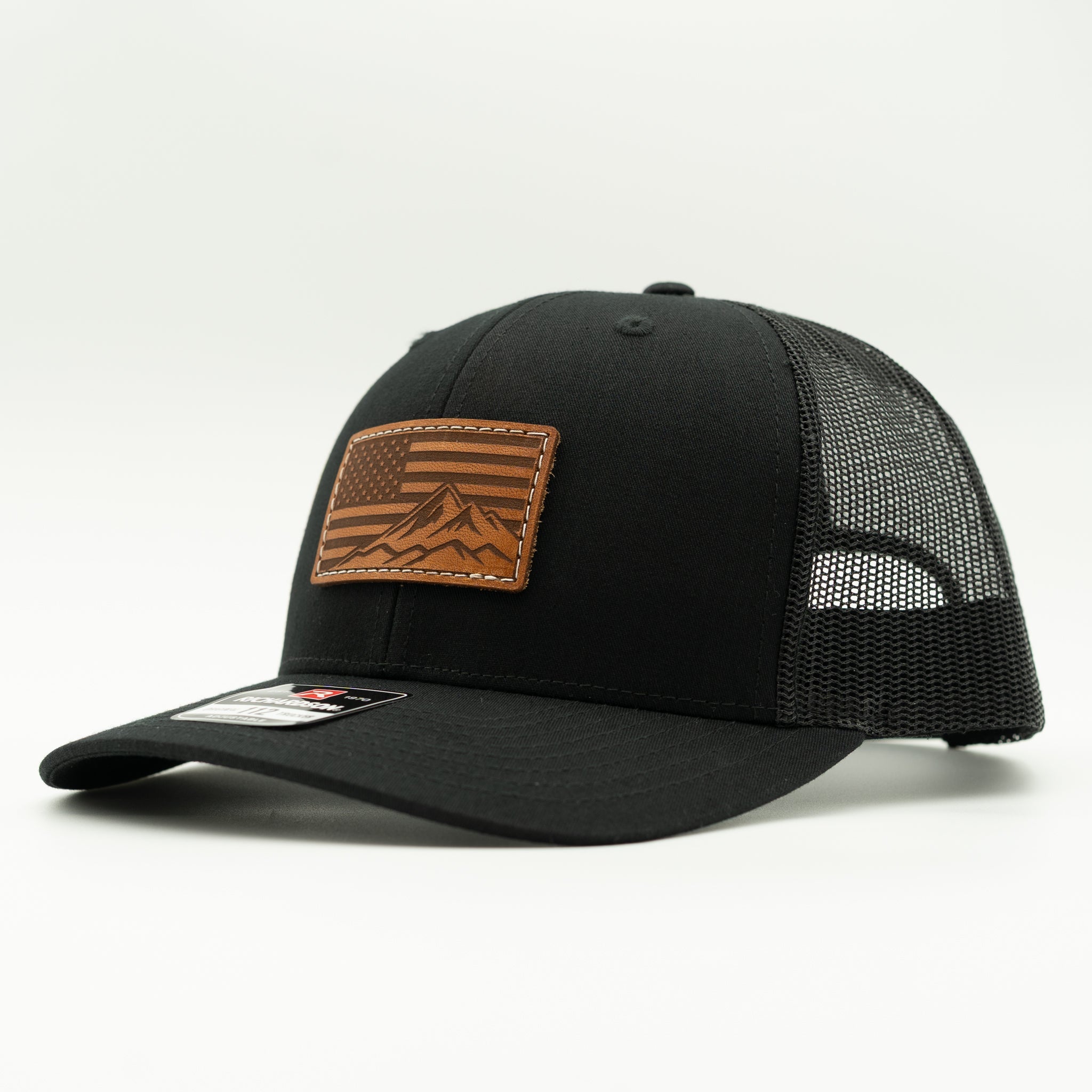 Side profile of American Range American flag leather patch hat on solid black Richardson 112 trucker, showing light brown patch, curved bill, mesh back, and snapback, a minimalist patriotic hat for mountain towns and outdoor lifestyles.
Color: Solid Black