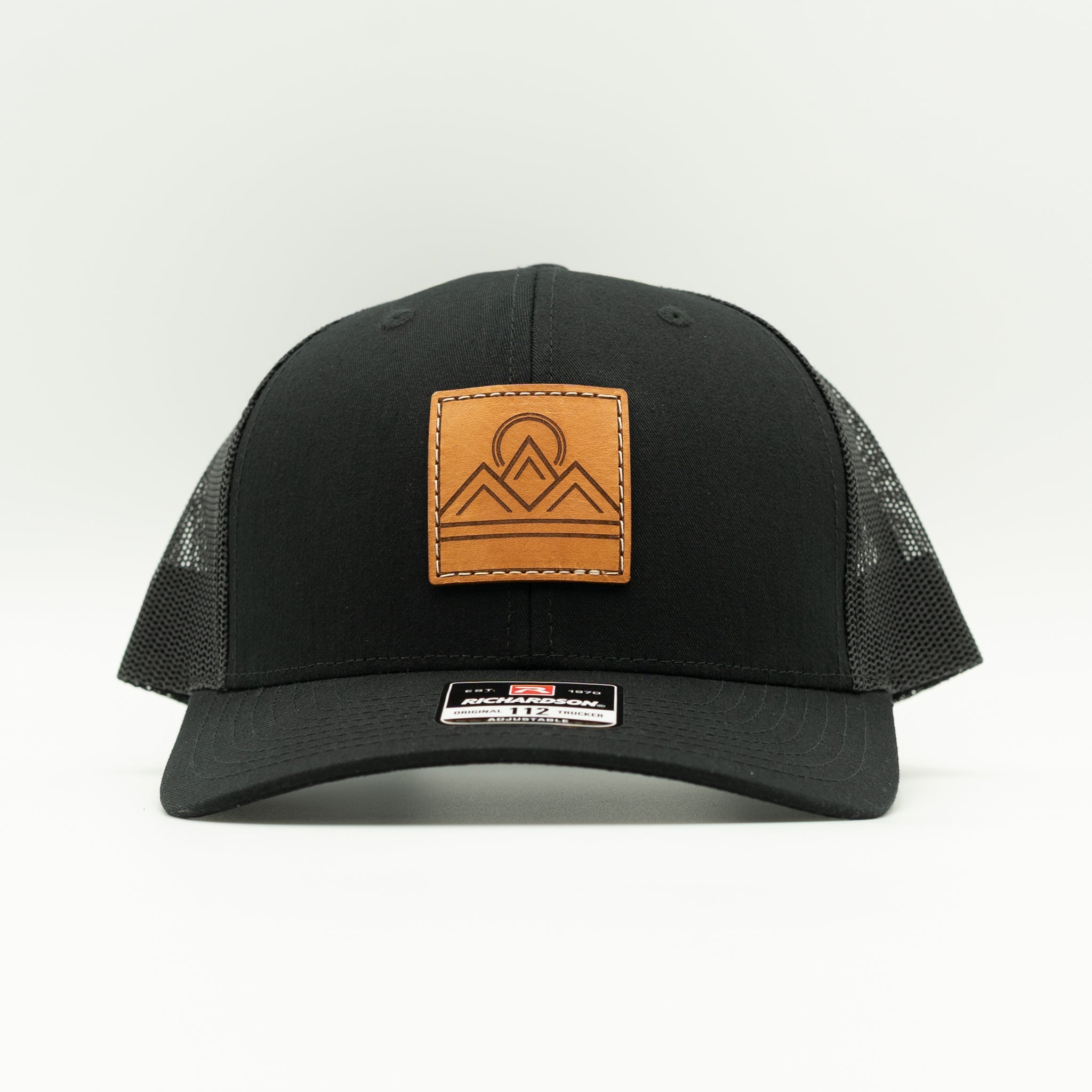 Front view of Lunar Ridge black on black Richardson 112 trucker hat with sewn veg tan leather mountain patch
Color: Solid Black