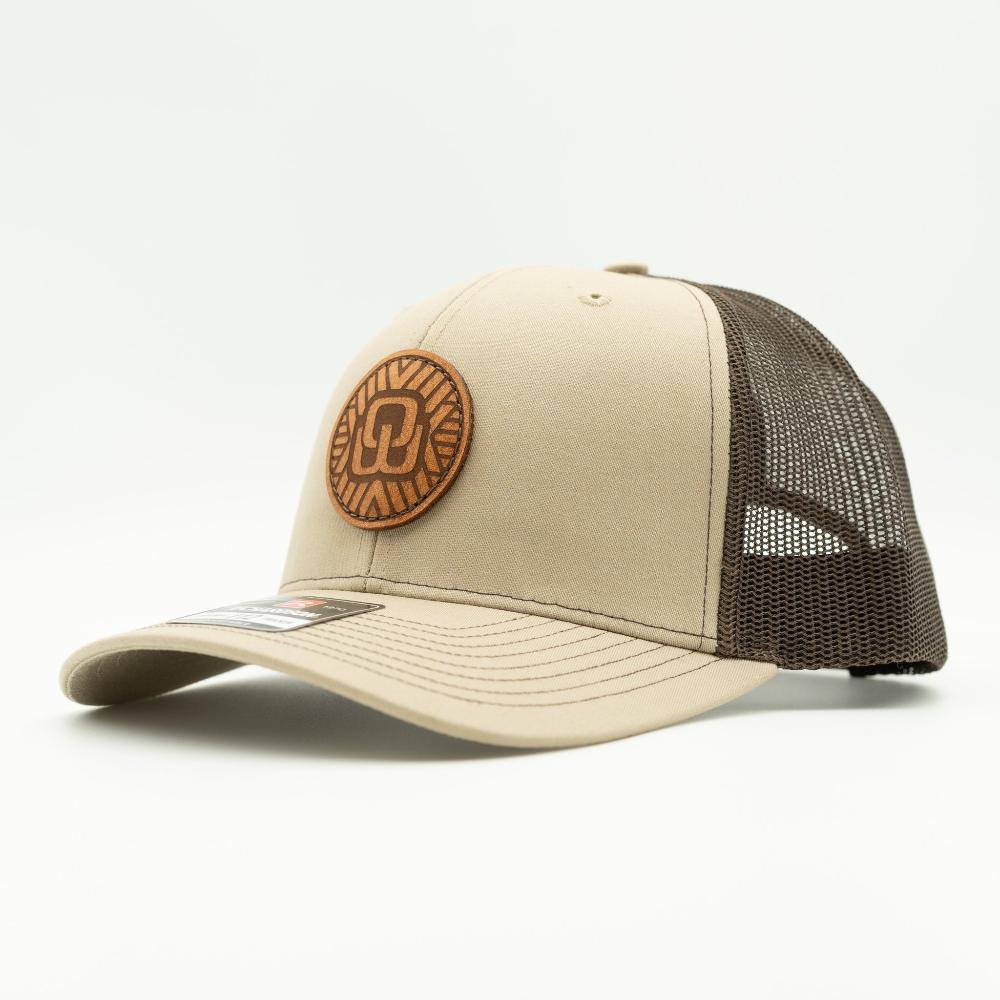A trucker-style baseball cap with a beige front panel and brim, dark brown mesh back panels, and a circular brown leather patch on the front.
Color: Khaki/Coffee