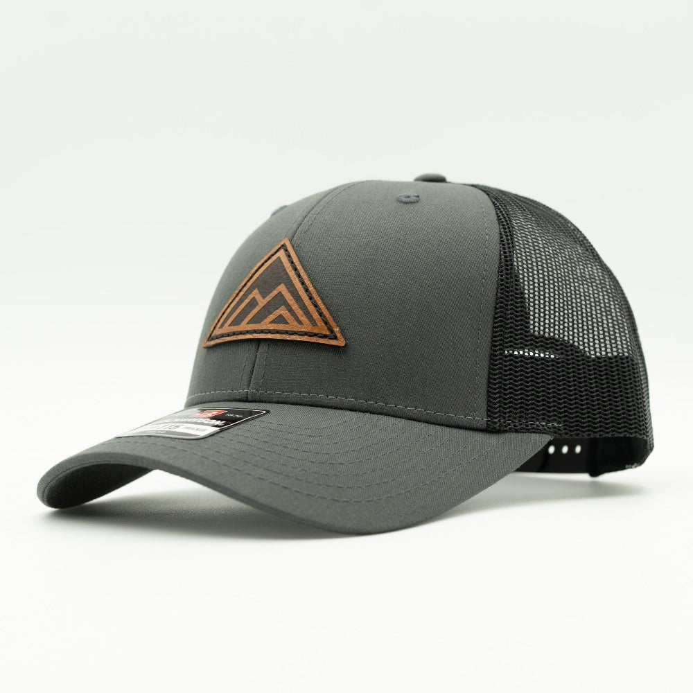 Side view of Dark Mountain leather patch hat on charcoal and black Richardson 115 low profile hat, showing triangle mountain patch, shallow crown, curved bill, and mesh back, a low profile mountain hat for hiking, camping, and travel.
Color: Charcoal/Black