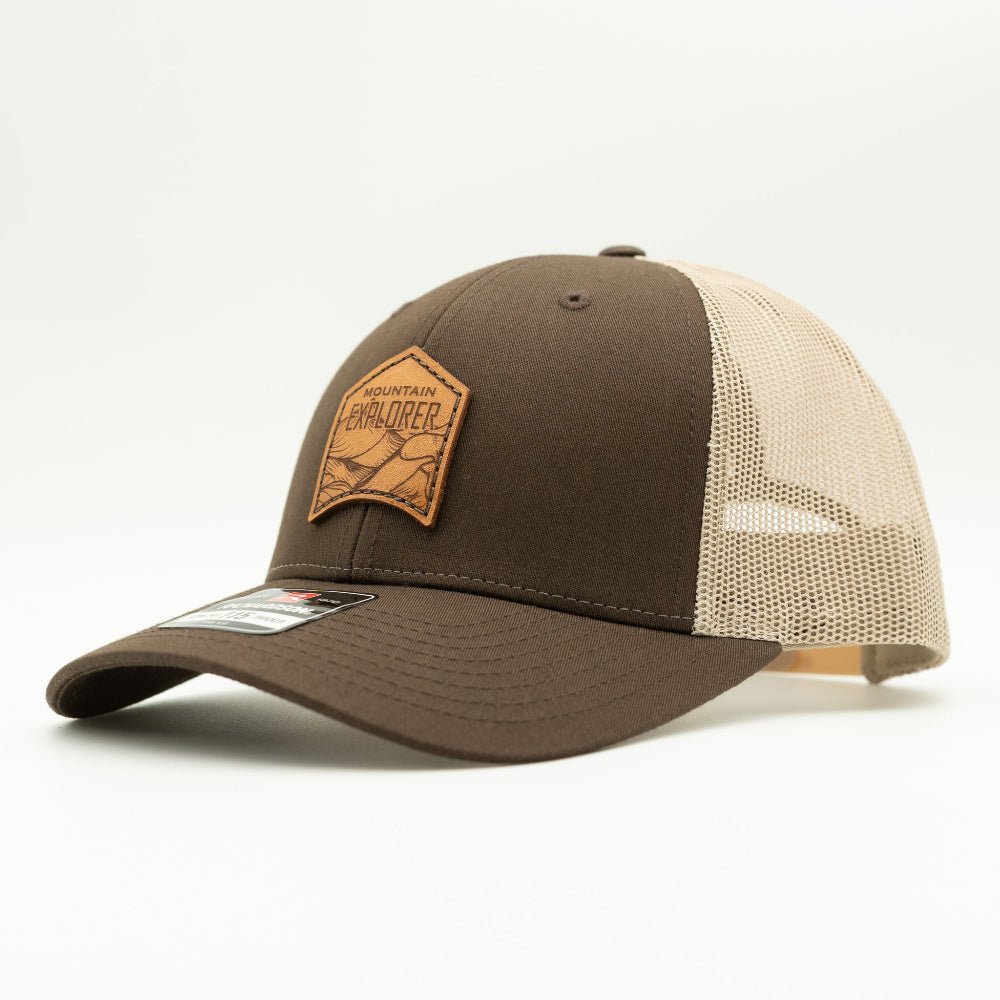 Side view of Mountain Explorer leather patch hat on brown and khaki Richardson 115 low profile trucker, showing warm two-tone crown, mesh back, and pre-curved visor.
