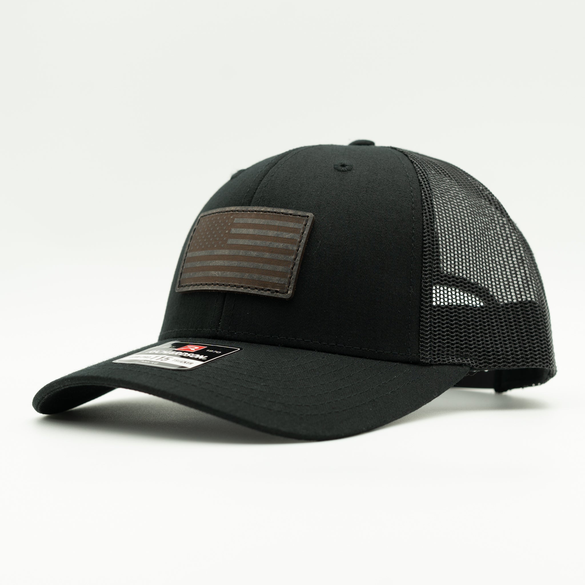 A black trucker-style baseball cap with a brown American flag patch on the front and a black mesh back, photographed on a clean white background.
Color: Solid Black