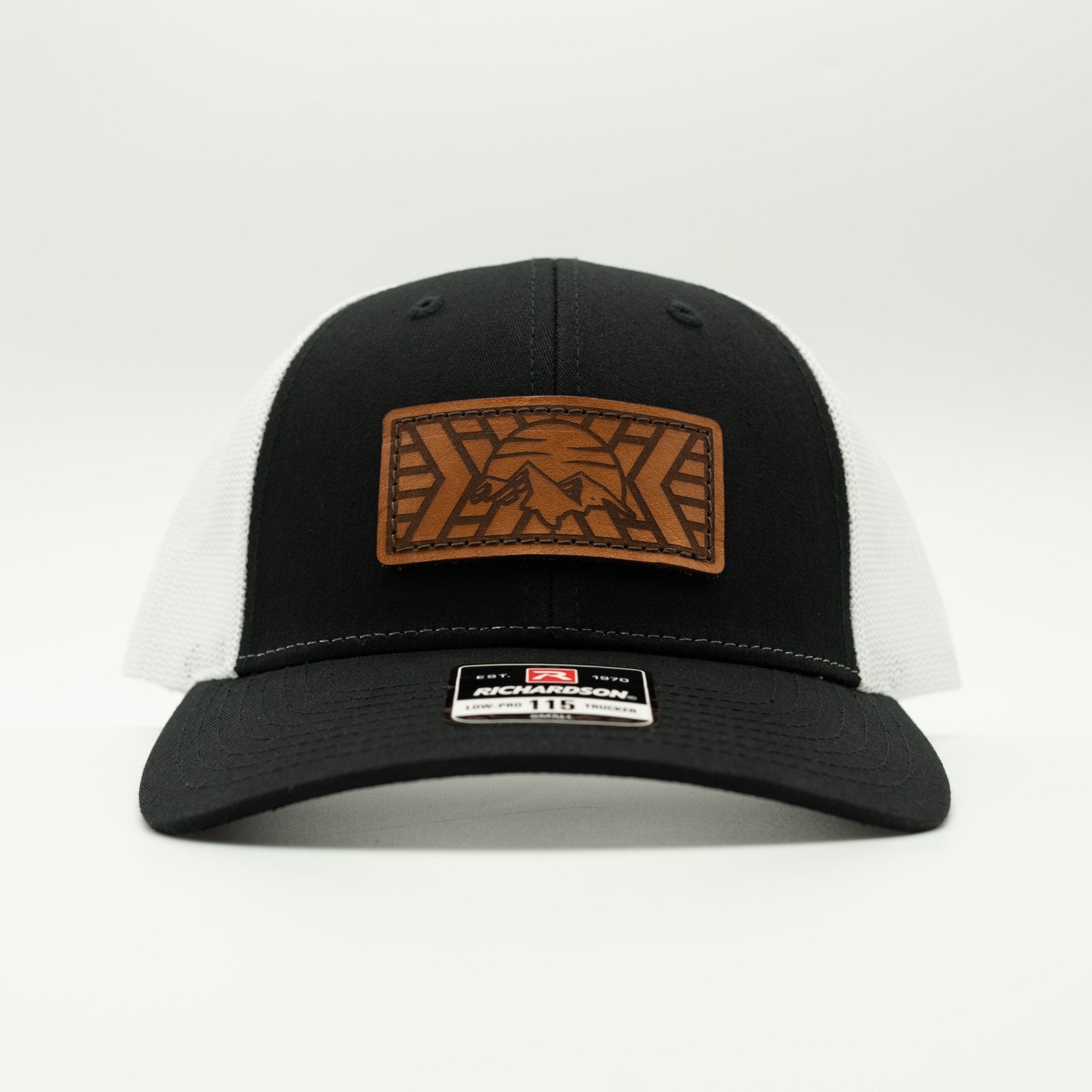 A black trucker hat with white mesh back panels and a brown leather patch on the front .
Color: Black/White