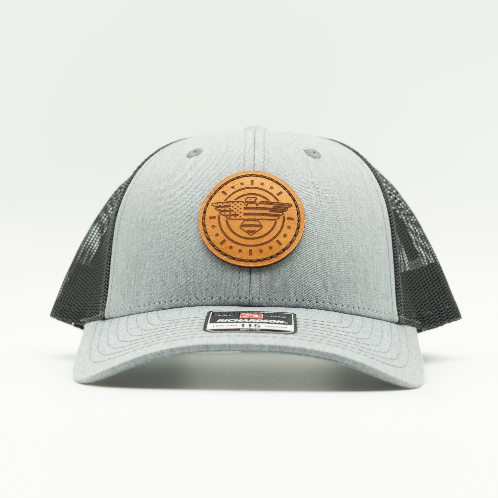 Front view of heather grey and charcoal Richardson 115 low profile trucker hat with engraved American Eagle and flag leather patch, curved visor, and dark mesh back.
Color: Heather Grey/Charcoal