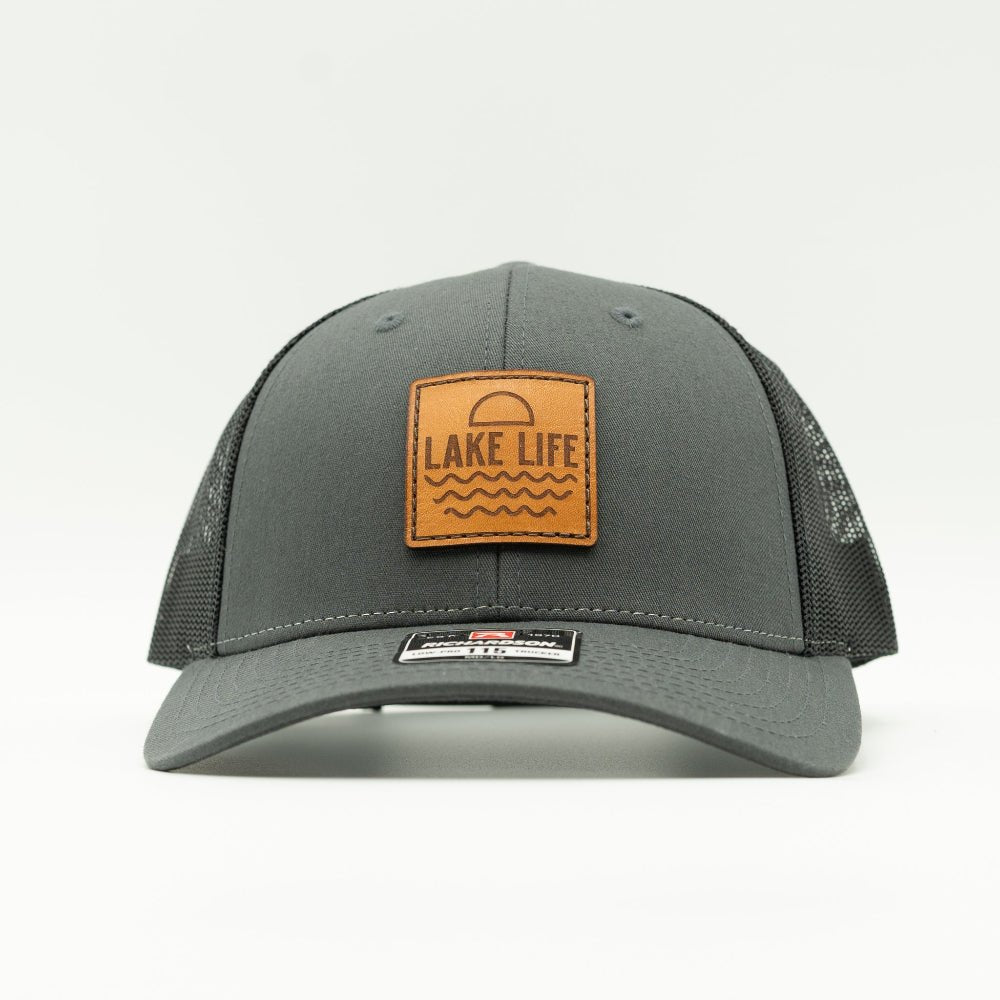 Front view of Lake Life leather patch hat on charcoal and black Richardson 115 low profile trucker, showing engraved leather patch, curved bill, mesh back, and snapback.
Color: Charcoal/Black