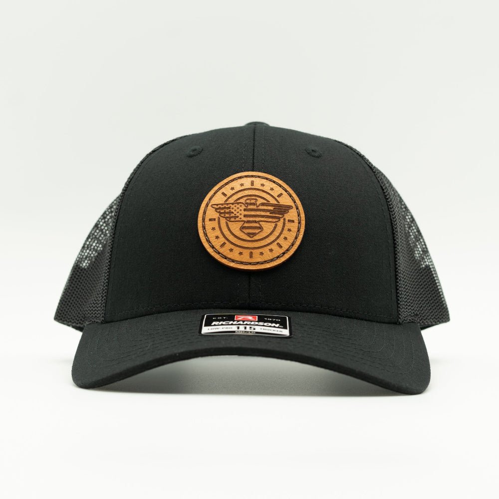 Front view of solid black Richardson 115 low profile trucker hat with round American Eagle and flag leather patch, curved visor, and breathable black mesh back.
Color: Solid Black