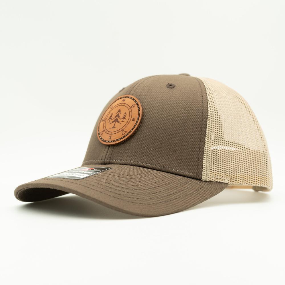 A trucker-style baseball cap with a solid brown front panel and brim, beige mesh back panels, and a circular brown leather patch on the front featuring a pine tree design.
Color: Brown/Khaki
