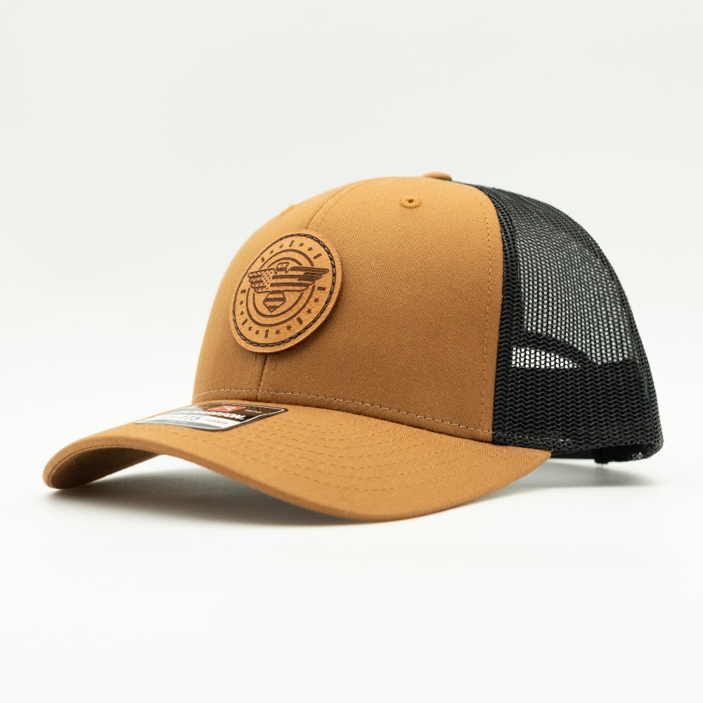 Side view of caramel and black Richardson 115 low profile trucker hat with American Eagle leather patch, showing warm caramel bill, shallow fit, and black mesh back.
Color: Caramel/Black
