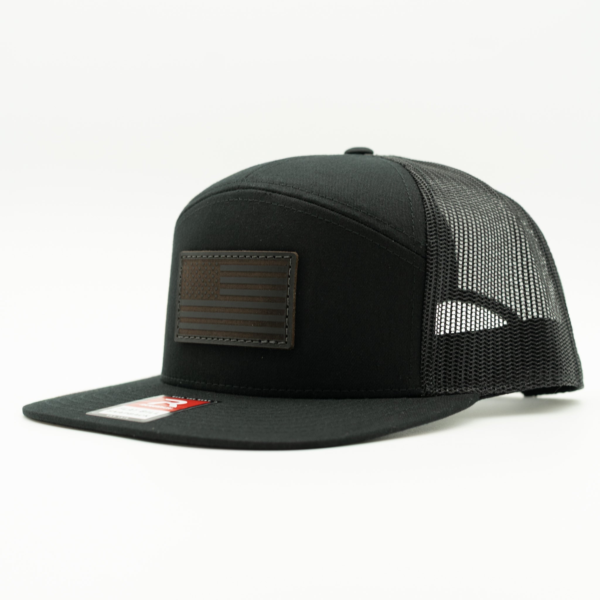 Solid black Richardson 168 seven panel trucker hat with black American Flag leather patch, side view showing flat bill, high profile fit, and mesh back.
Color: Black/Black 168 (OSFM)