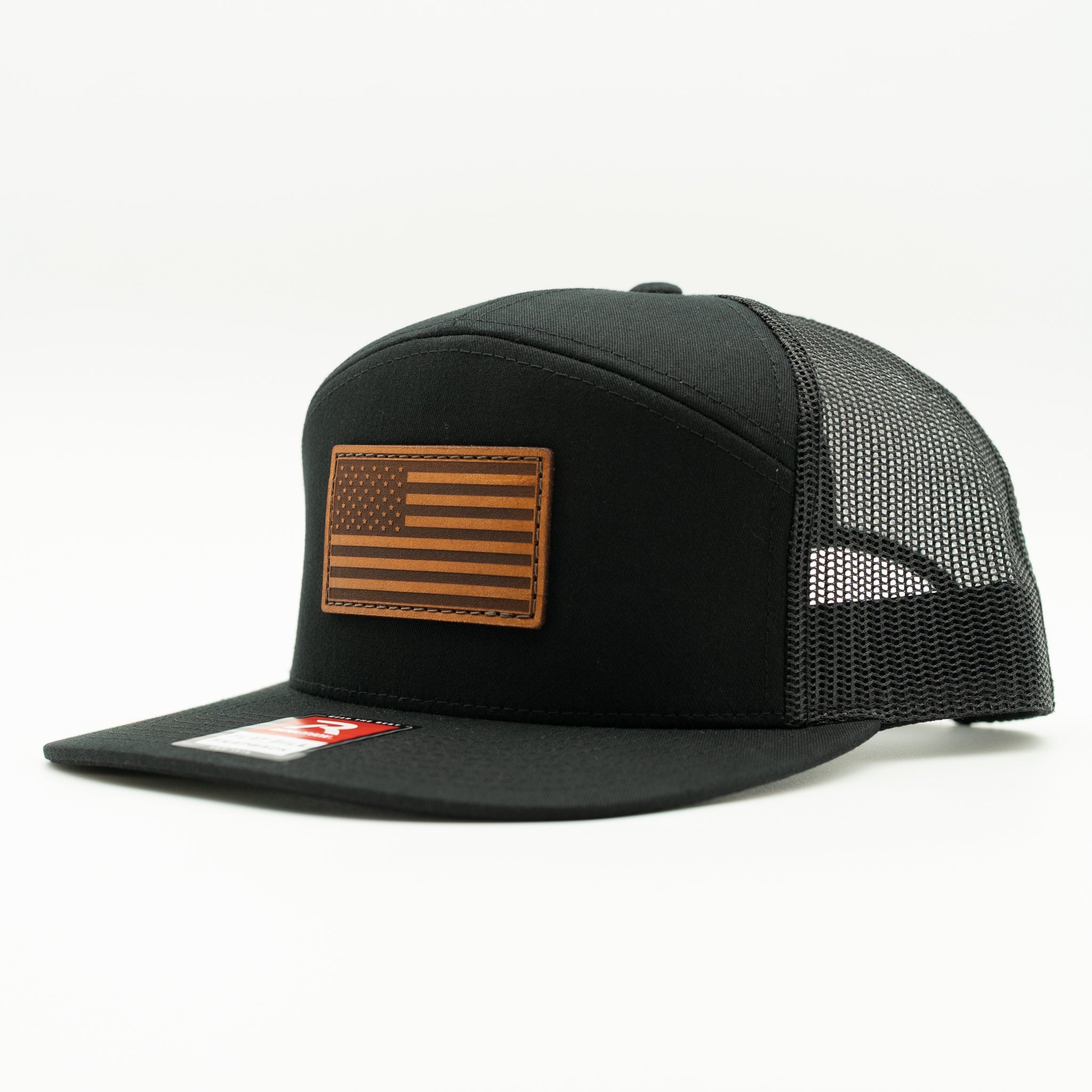 Solid black Richardson 168 seven panel flat bill trucker hat with light brown American Flag leather patch, side view showing high crown and mesh back.
Color: Black/Black 168 (OSFM)