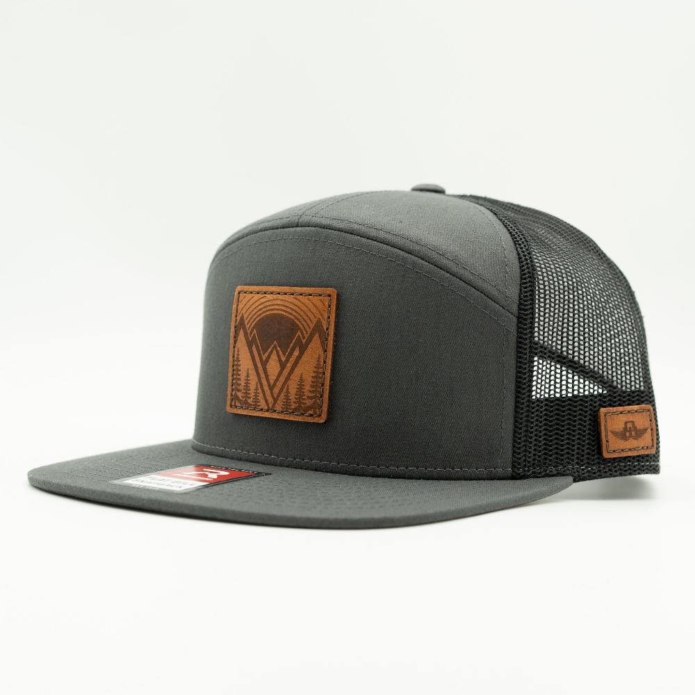 Side view of Mountain East leather patch hat on charcoal and black Richardson 168 flat bill trucker, highlighting the sewn veg tanned mountain patch and mesh back.