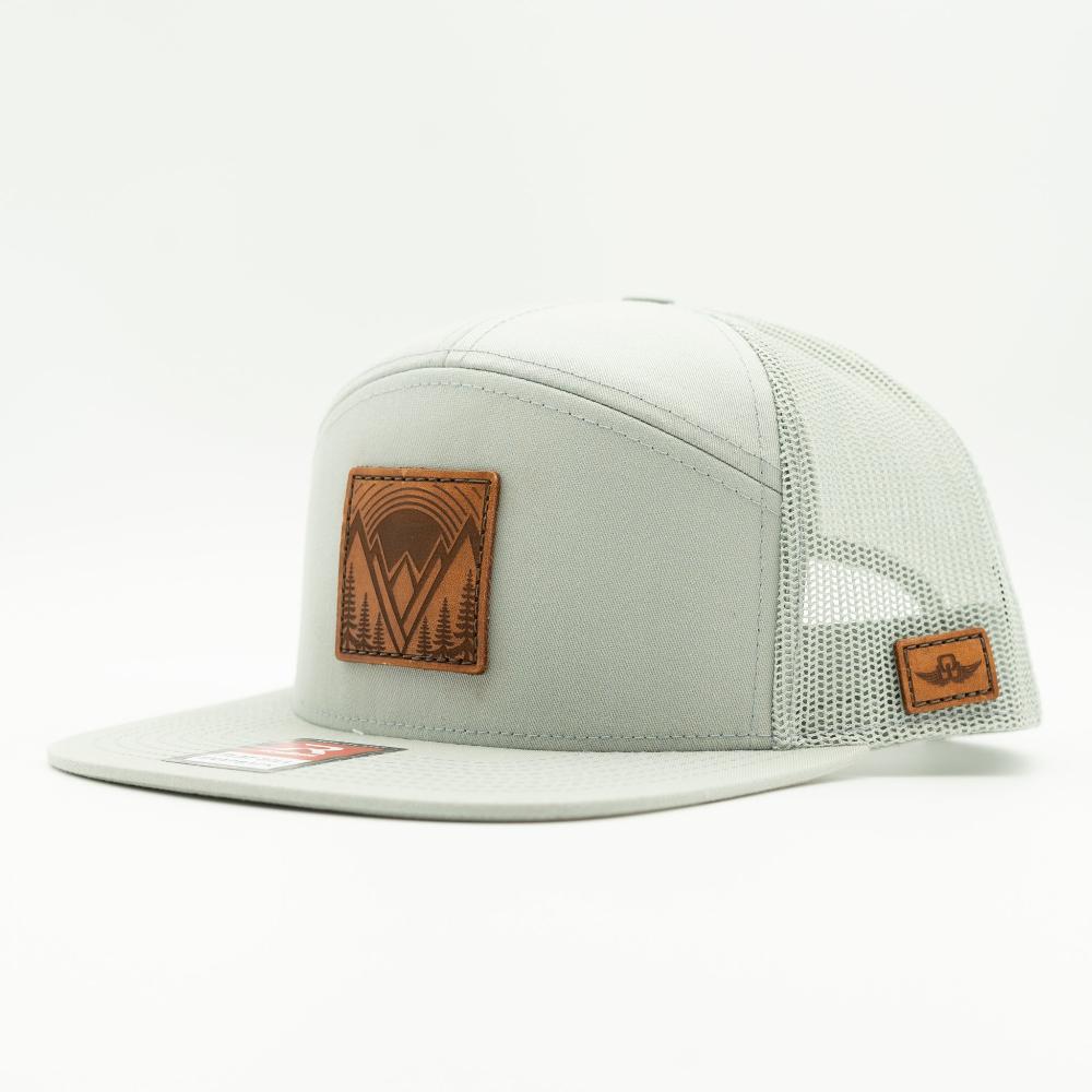 Side view of Mountain East leather patch hat on quarry gray Richardson 168 flat bill trucker, showing seven panel shape, mesh back, and sewn leather mountain patch.