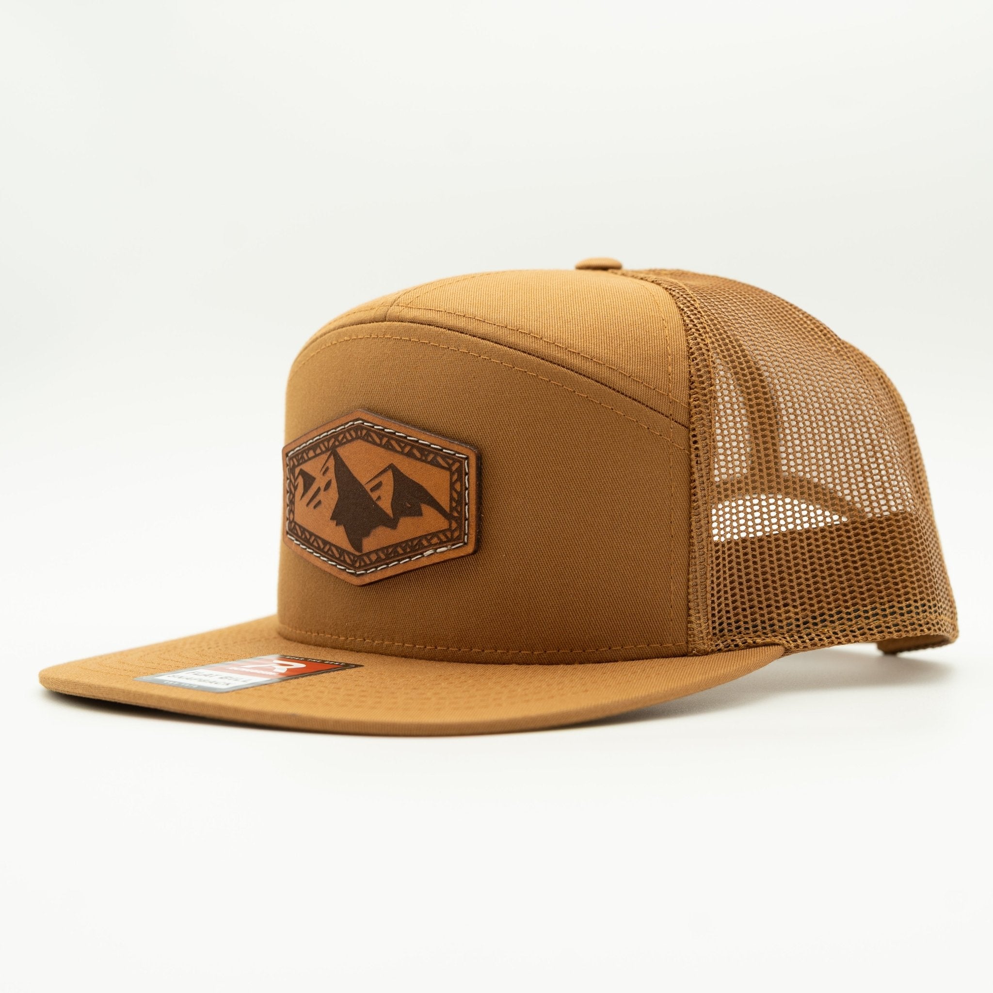 A tan trucker hat with a structured front panel, matching flat brim, and tan mesh back. It features a brown leather patch on the front with a mountain logo.
Color: Caramel 168 (OSFM)