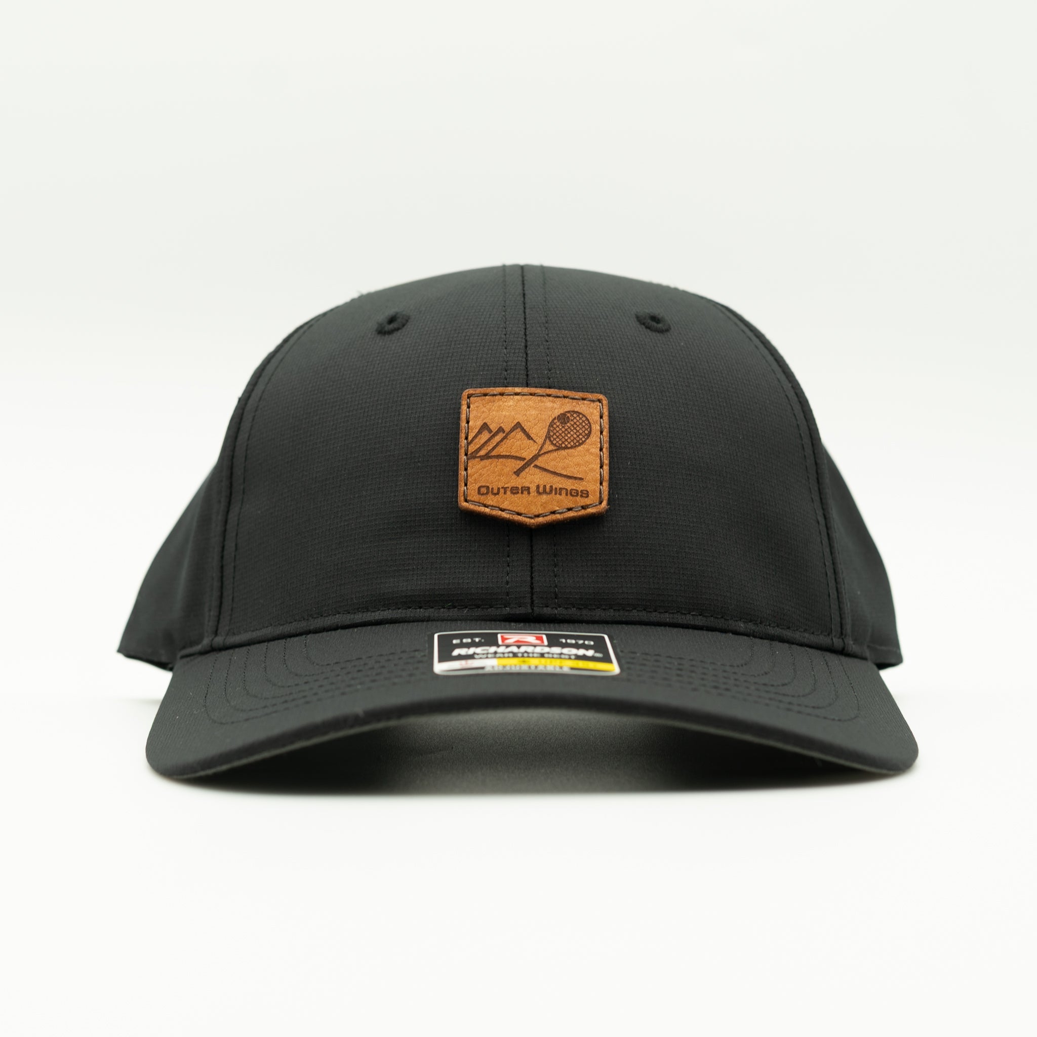 A black baseball cap with a brown leather patch on the front featuring a mountain and tennis racket design, with the brand name 'Outer Wings' printed on it. The cap is photographed against a clean white background.
Color: Black