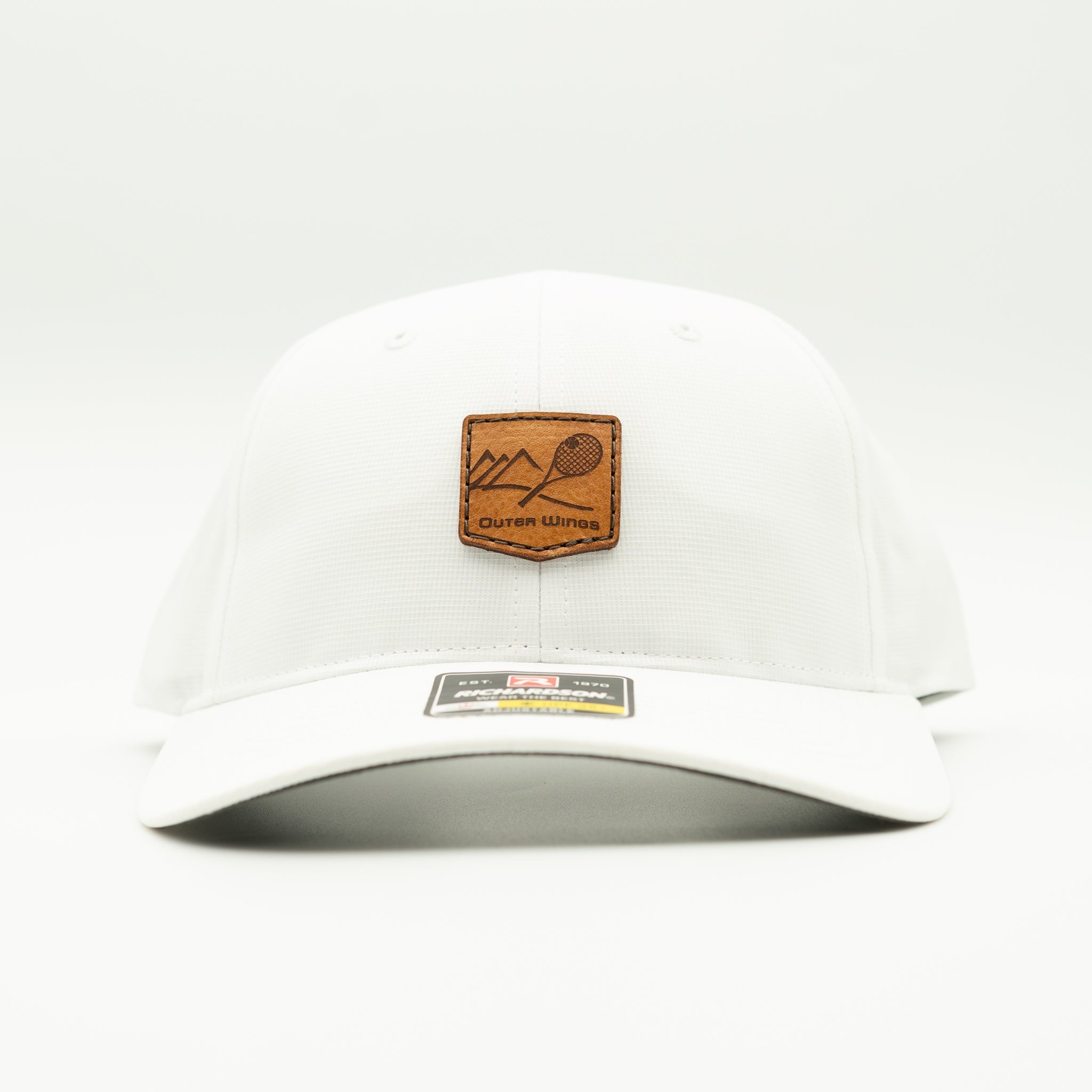 A white structured baseball cap with a brown leather patch on the front featuring a mountain and racket design, with the text 'Outer Wings' on the patch and a size/brand sticker on the brim.
Color: Solid White