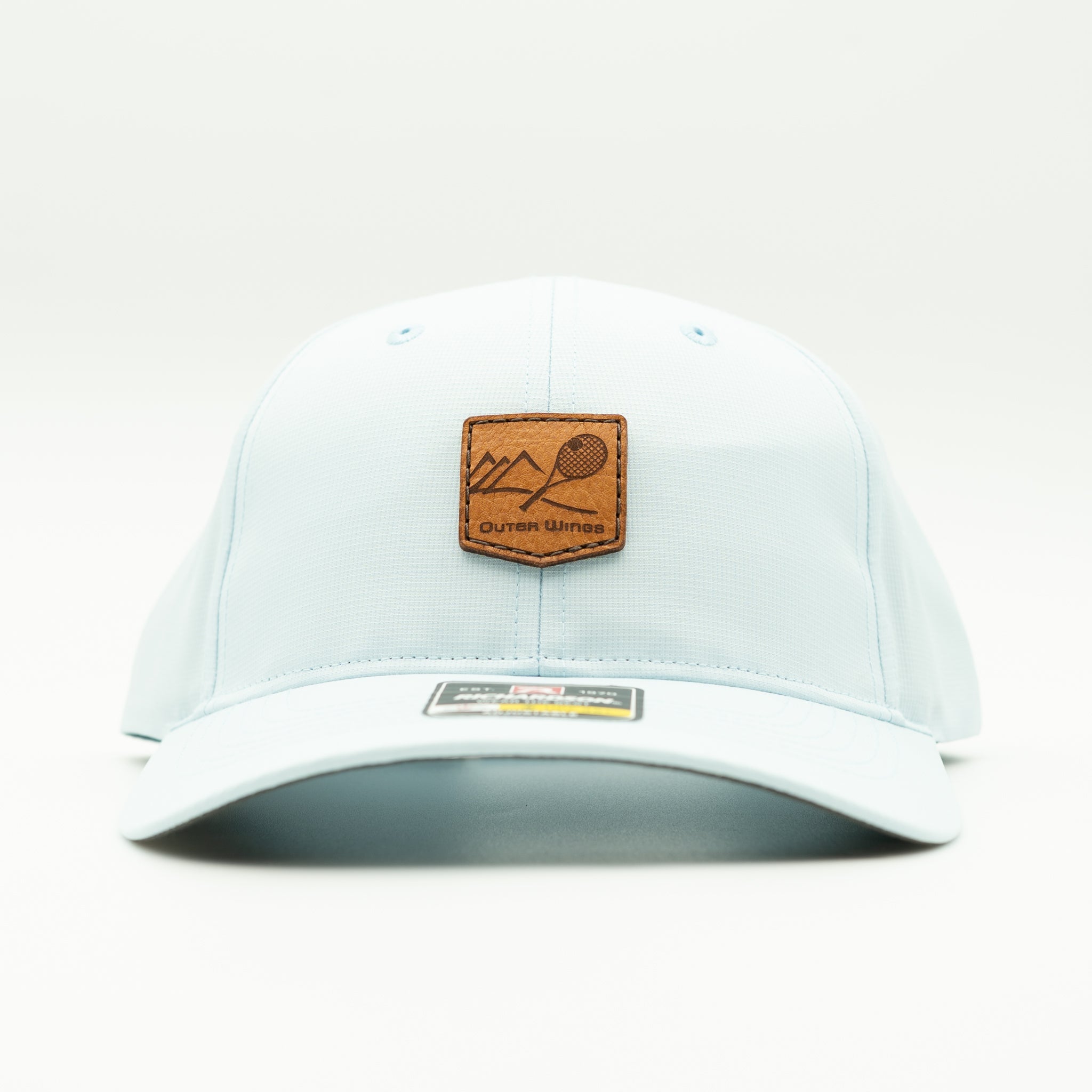 A light blue structured baseball cap with a brown leather patch on the front featuring a mountain and racket design, with the text 'Outer Wings'.
Color: Soft Blue