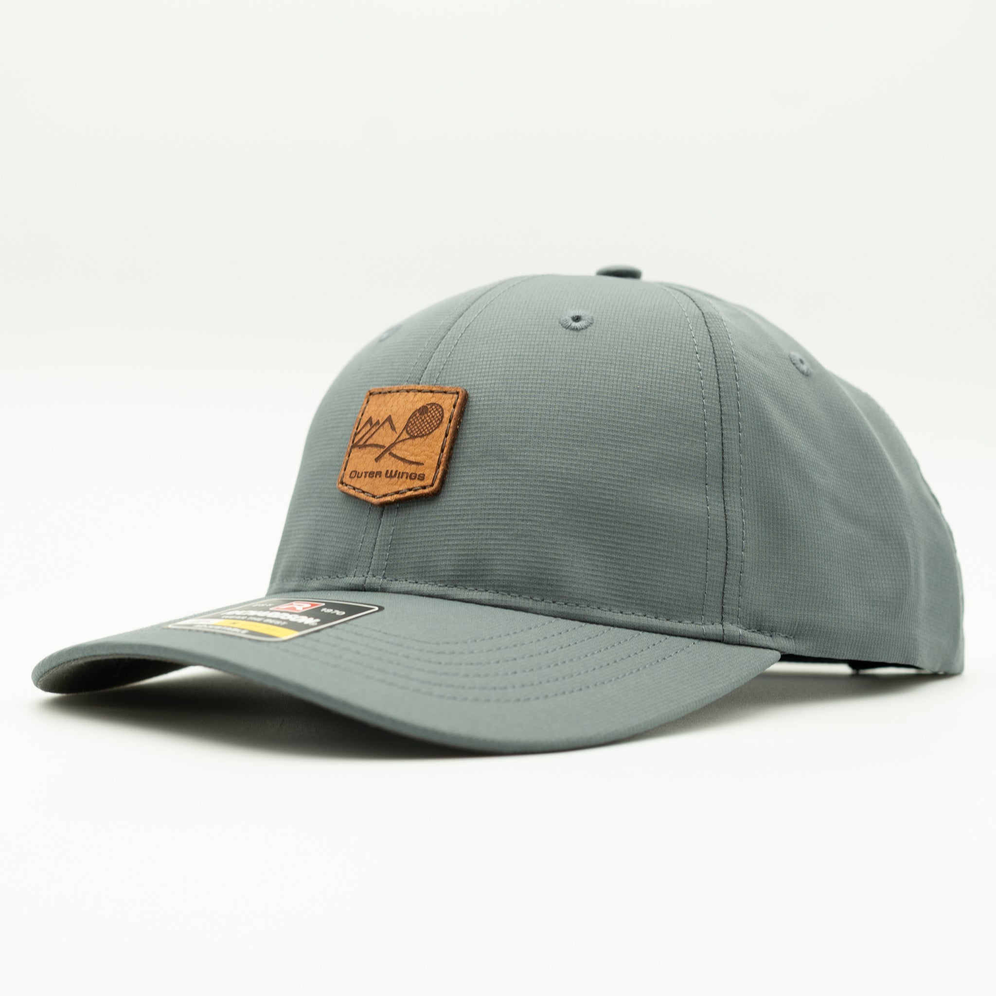 A slate gray baseball cap with a brown leather patch on the front featuring a mountain and tennis racket design, photographed on a clean white background.
Color: Dark Grey