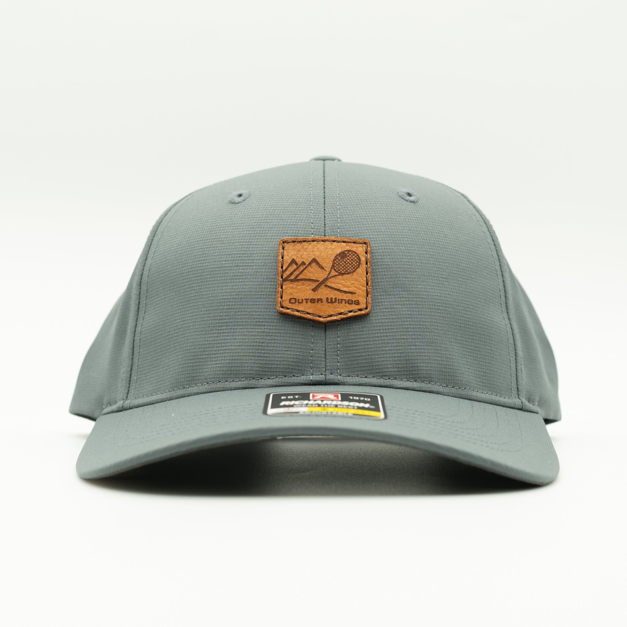 A gray structured baseball cap with a brown leather patch on the front featuring a mountain and paddle graphic, with the text 'Outer Wings' on the patch and a size/brand sticker on the brim.
Color: Dark Grey