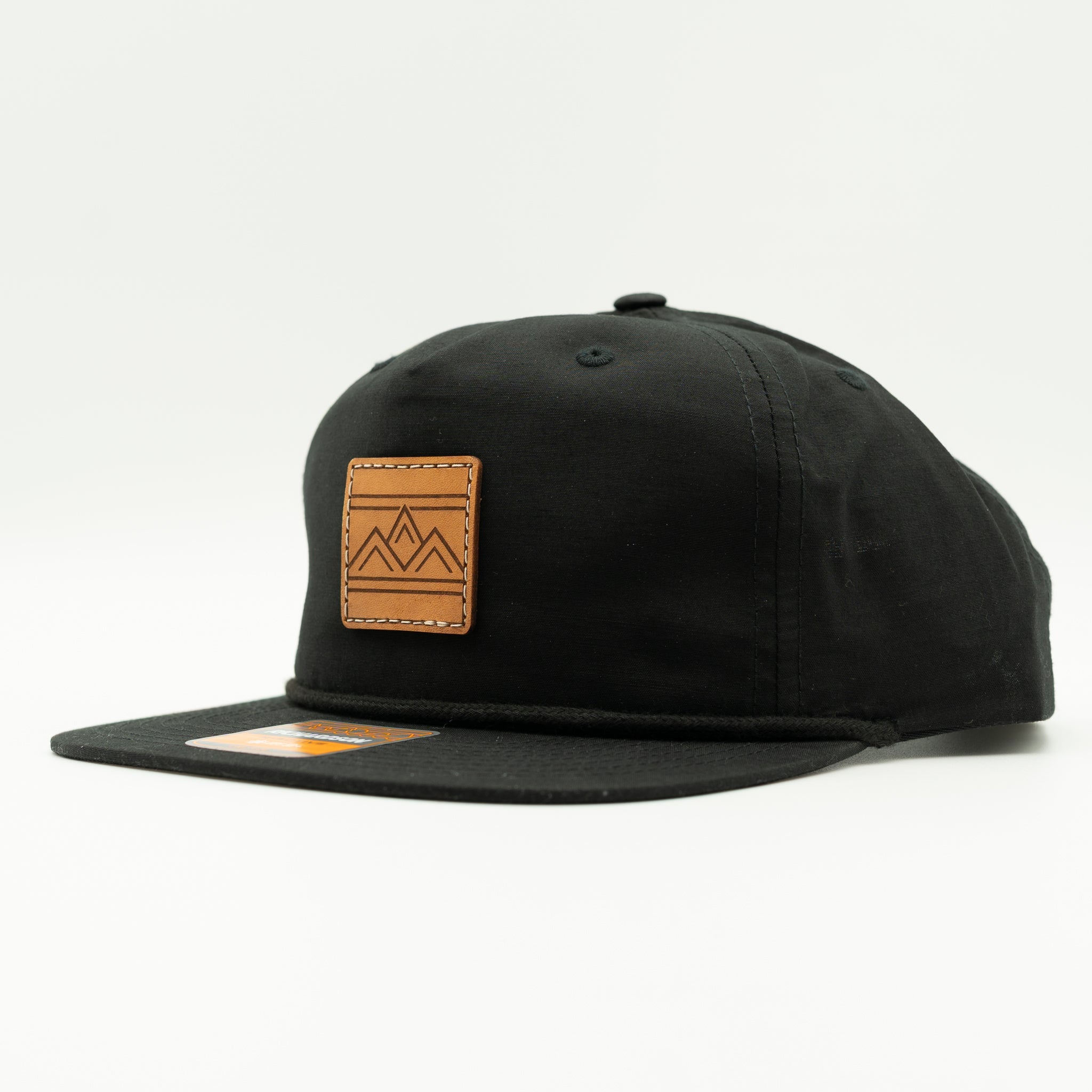 Rustic Ridge Richardson 256 black rope hat side view, showing low profile five-panel shape, flat bill, and square leather mountain patch.