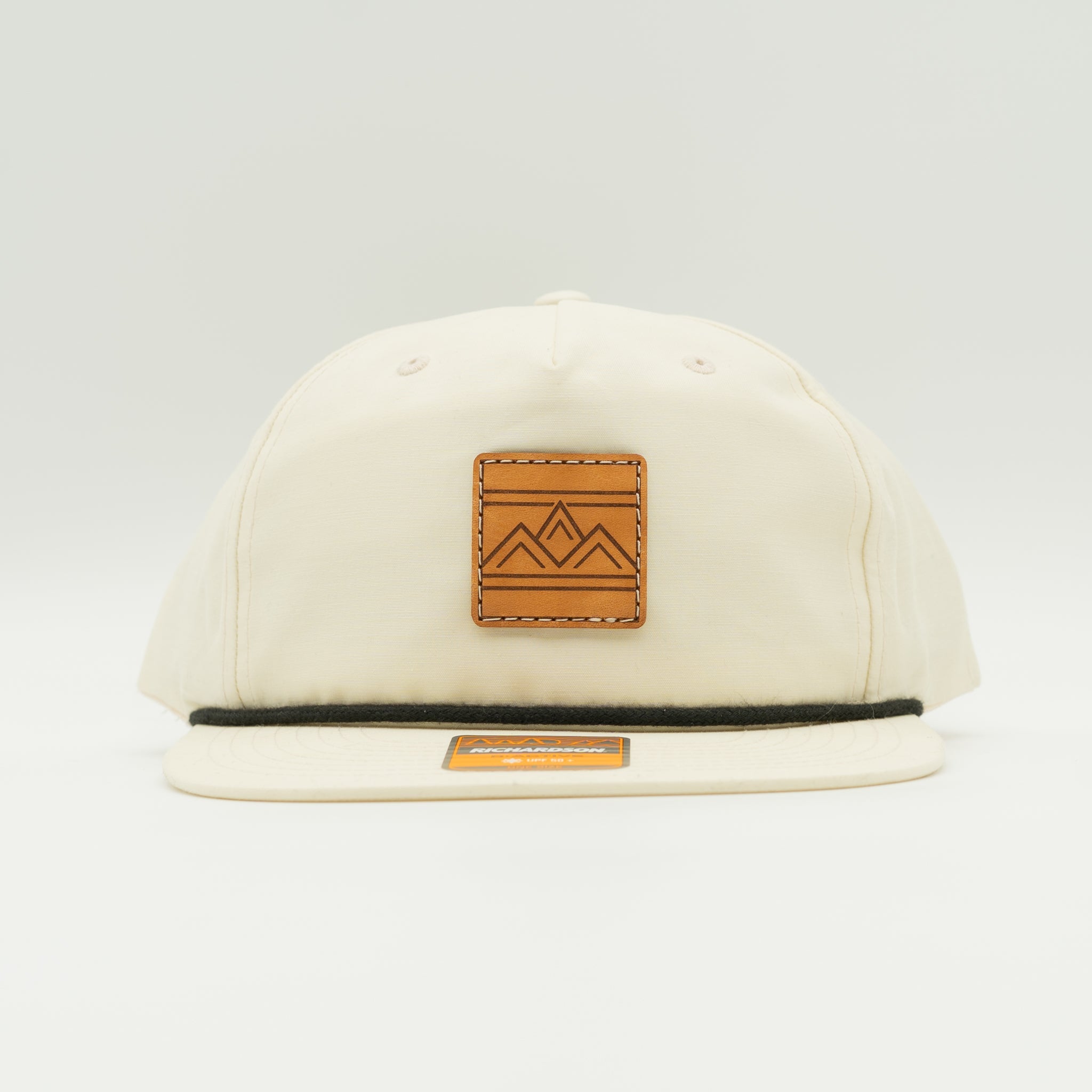 Rustic Ridge birch and black Richardson 256 rope hat front view, featuring square veg tan leather three-peak mountain patch and flat bill.