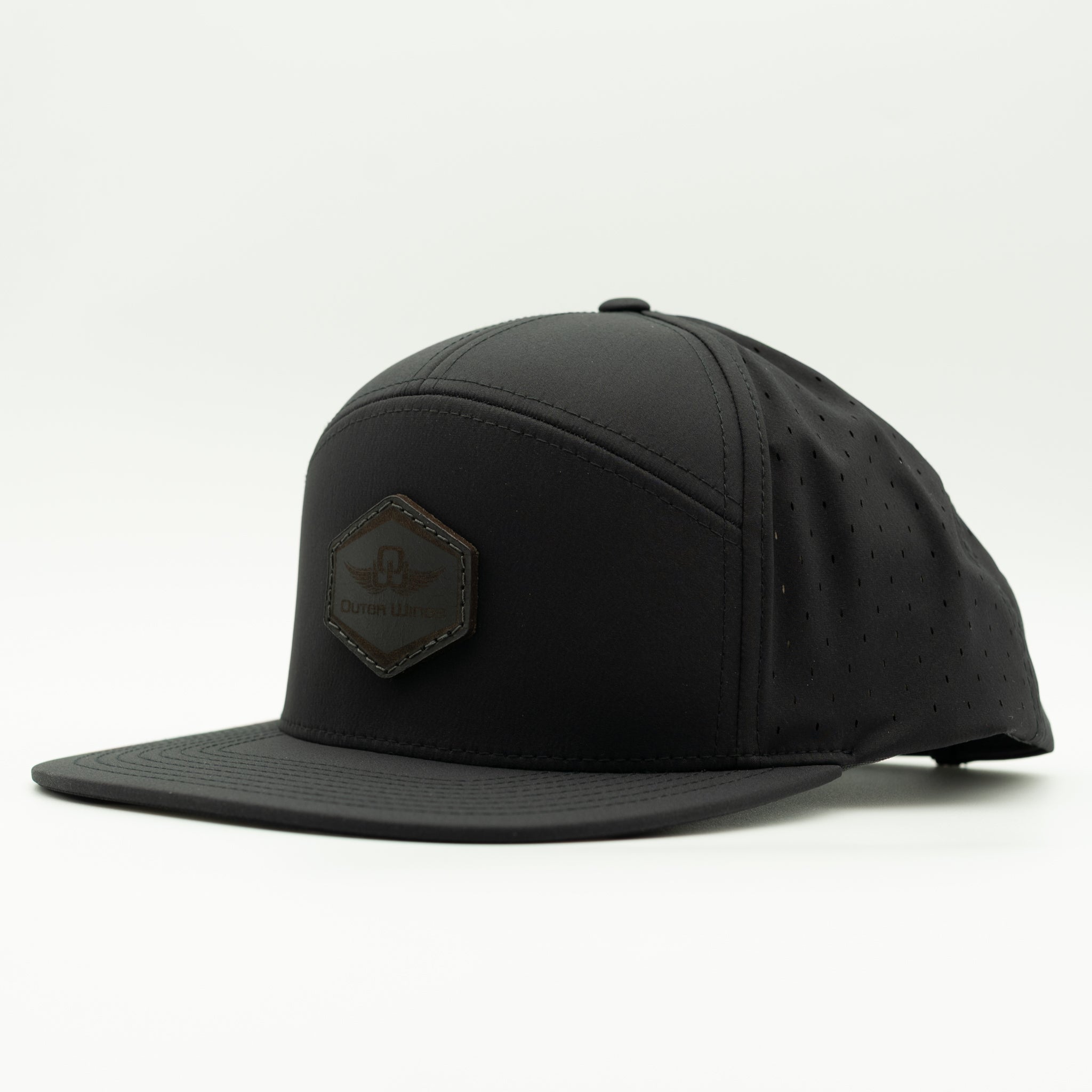A black flat-brim cap with a structured crown, perforated side panels, and a dark brown hexagonal patch on the front featuring the 'Cruiser USA' logo, set against a plain white background.
Color: Black