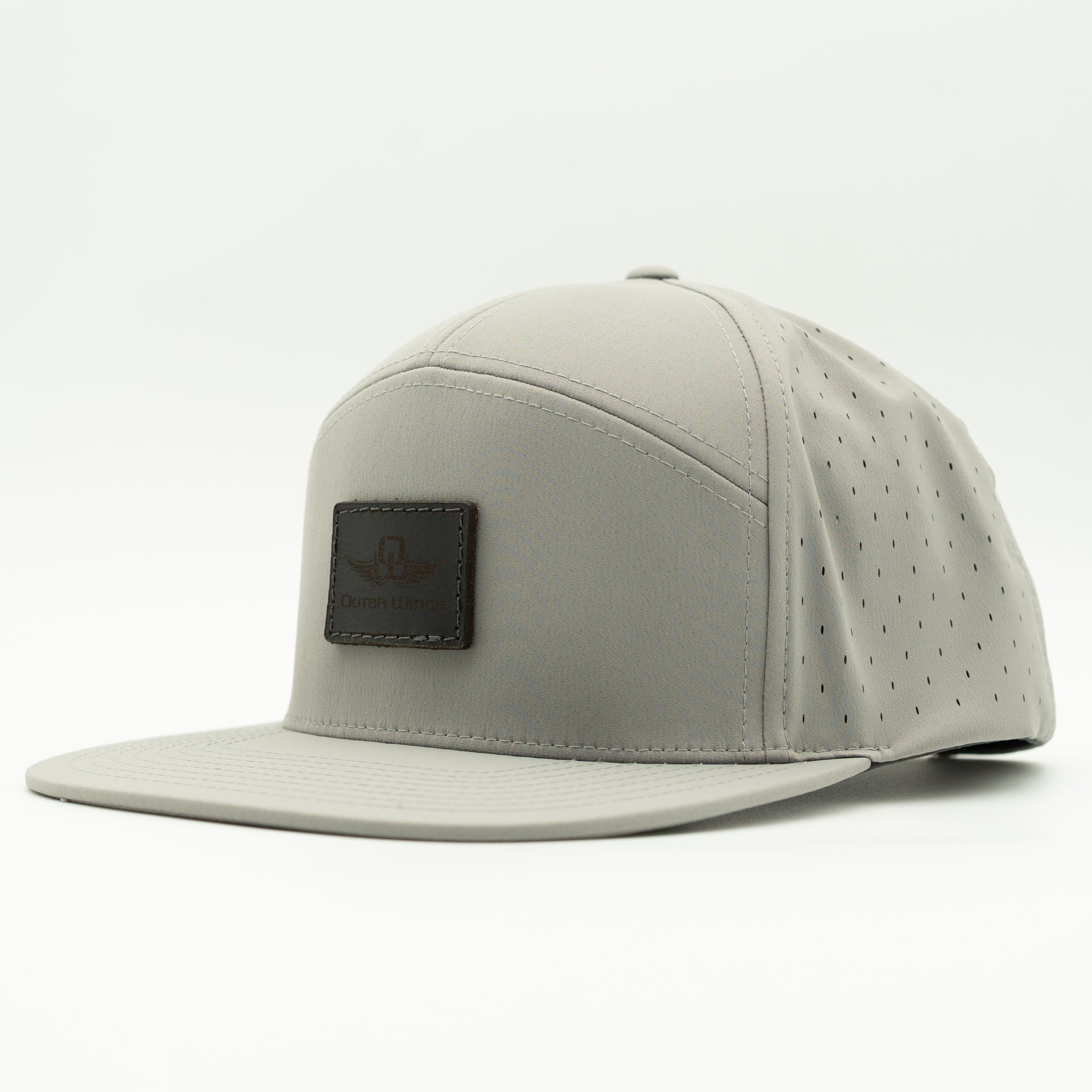 A light gray flat-brim cap with perforated side panels and a dark brown rectangular patch on the front, photographed on a clean white background.
Color: Silver